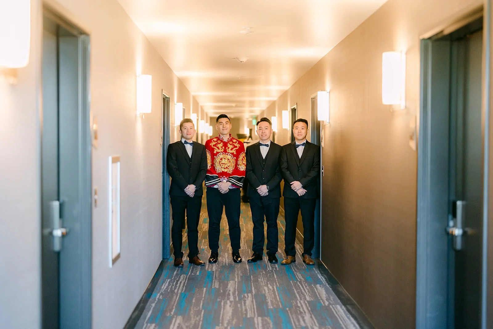 The groom and his groomsmen lined up in a hotel hallway on their way to the bride's door.