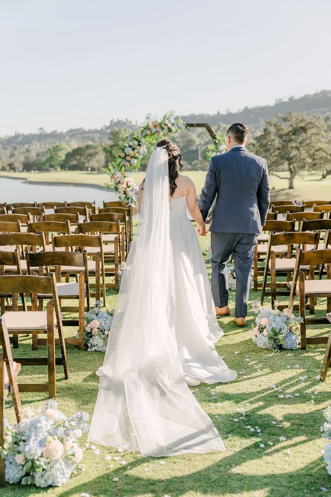 Florence and Jordan walking down the aisle of wooden chairs before the ceremony