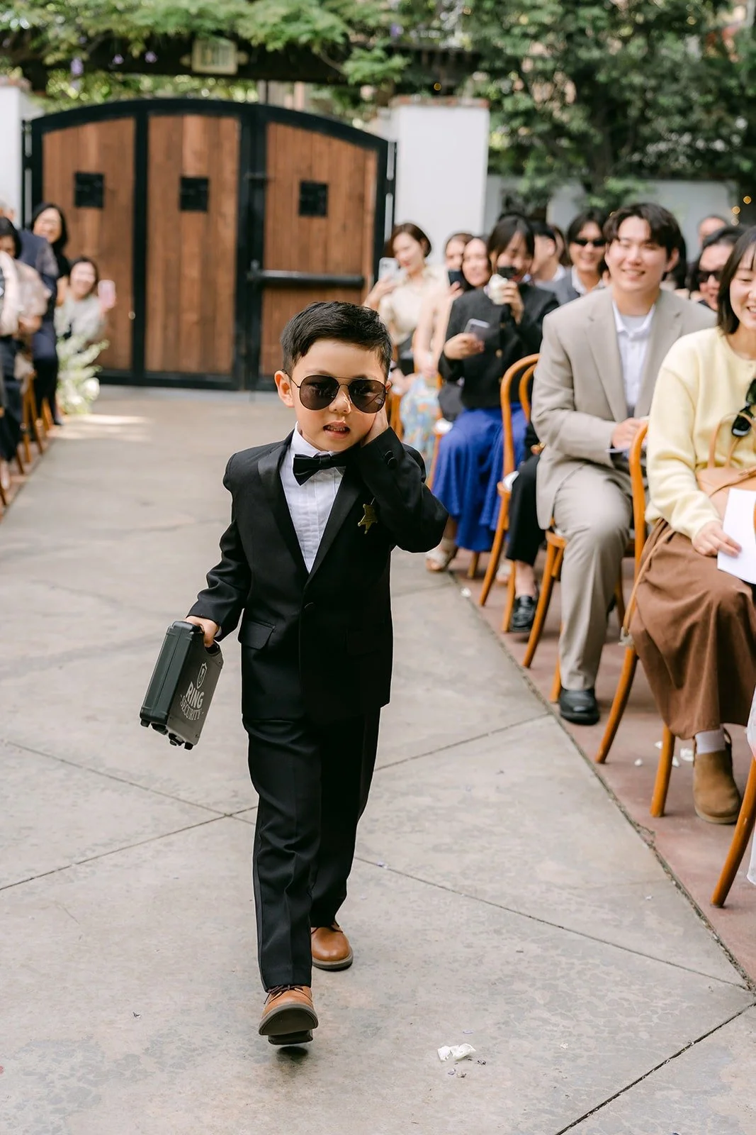 A young ring bearer walking down the aisle in sunglasses