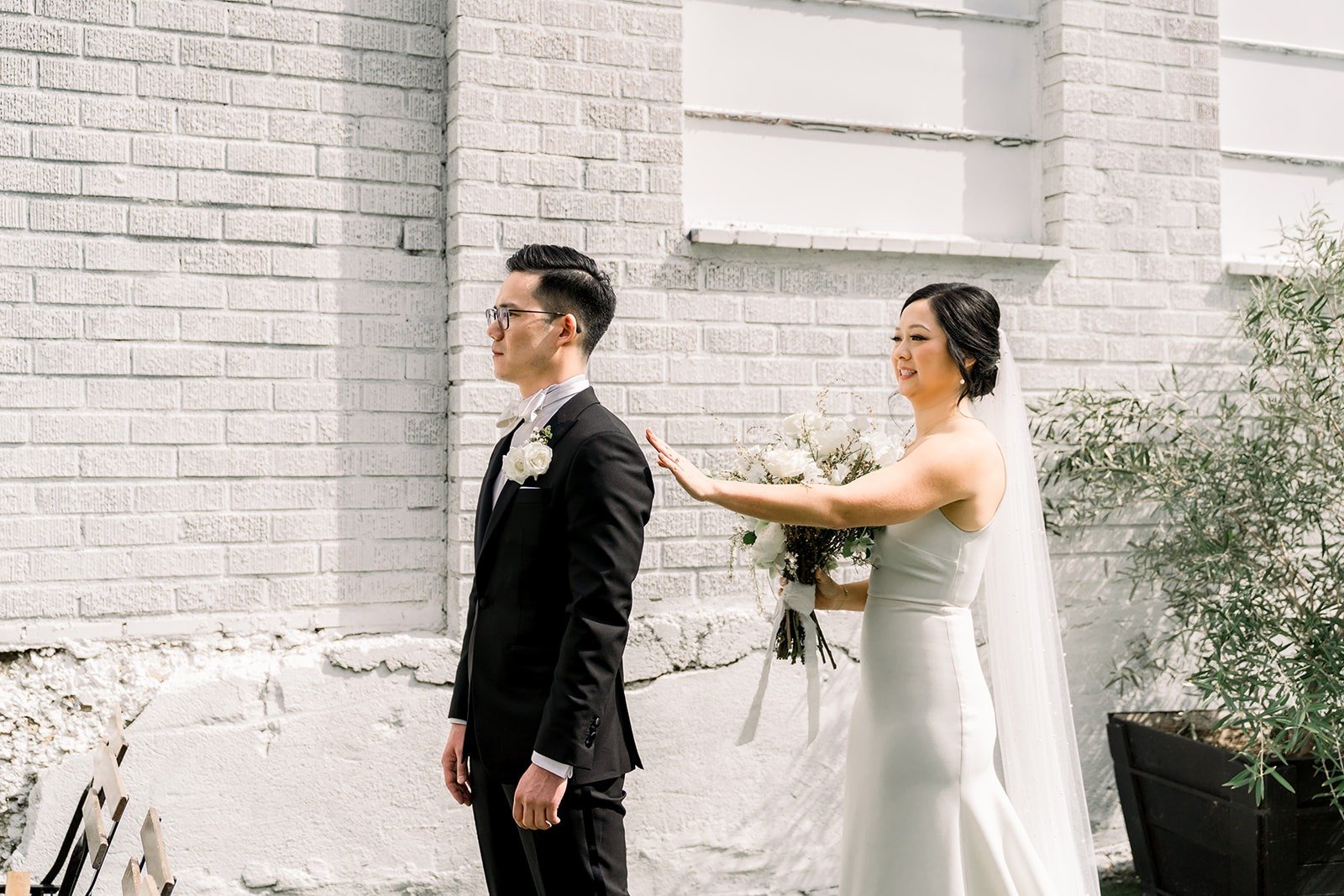 Cindy walks up to Alex beside the white brick wall