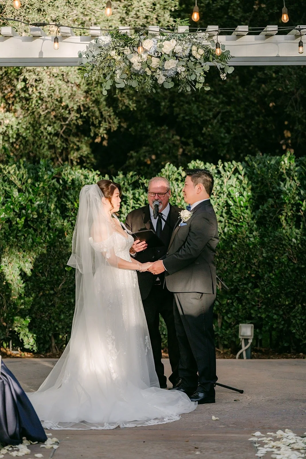 Sochi and Jay hold hands at the arbor with the officiant