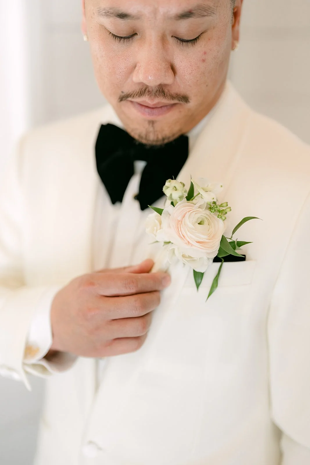 Close up of Caryl adjusting his boutonniere on his white dinner jacket and black bow tie.