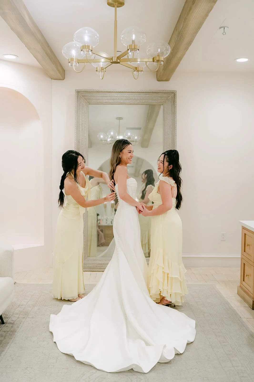 Bridesmaids in butter yellow dresses fluffing the bride's train in the bridal suite
