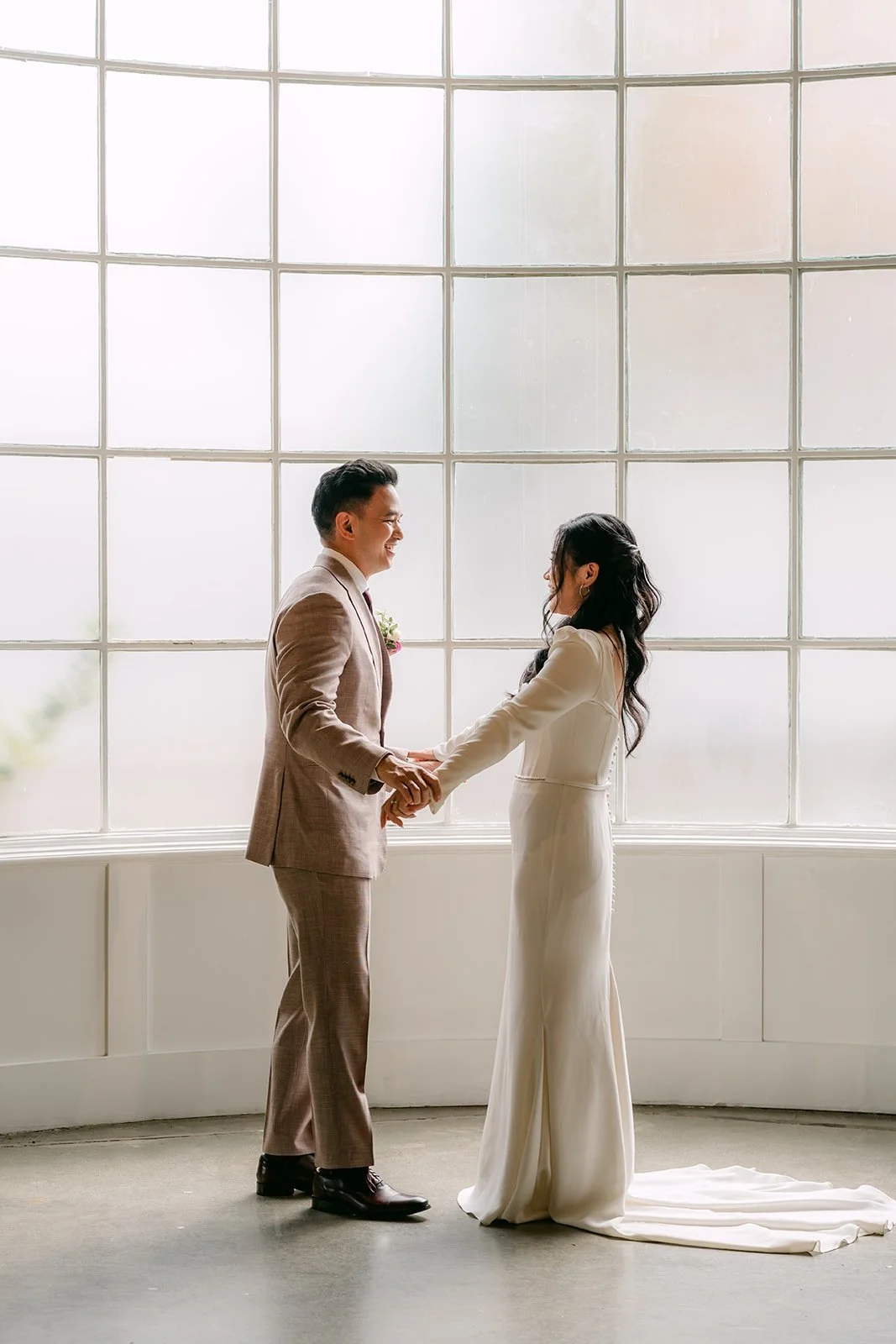 Michael and Denise holding hands in front of the window wall during their first look.