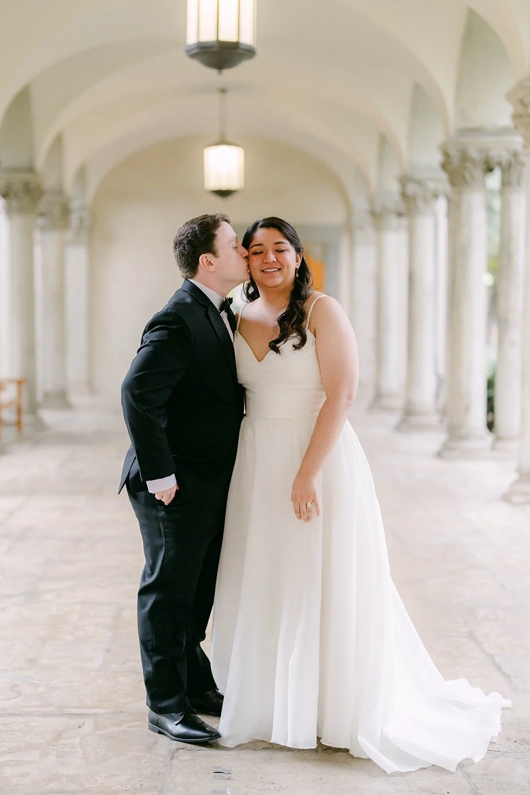 Saira and Matthew laughing in the arcade of columns and lanterns at The Athenaeum in Pasadena