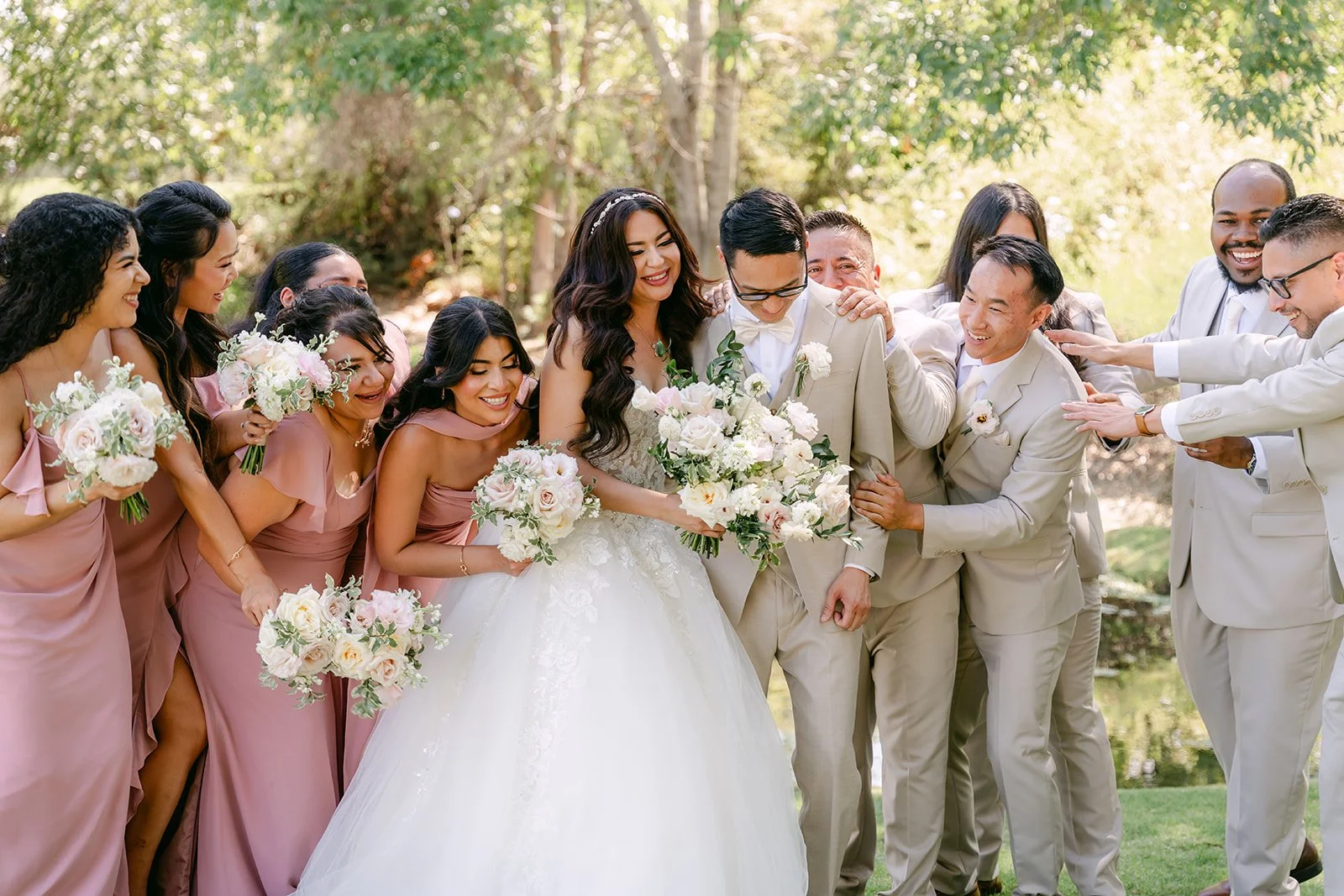 Sandra and Kevin laughing with their wedding party under the trees.