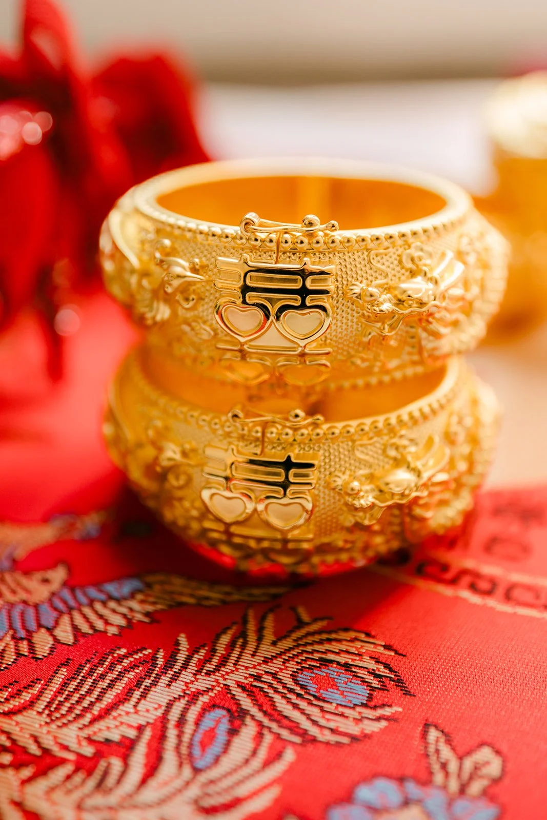 A stack of thick gold wedding bangles on red embroidered fabric.