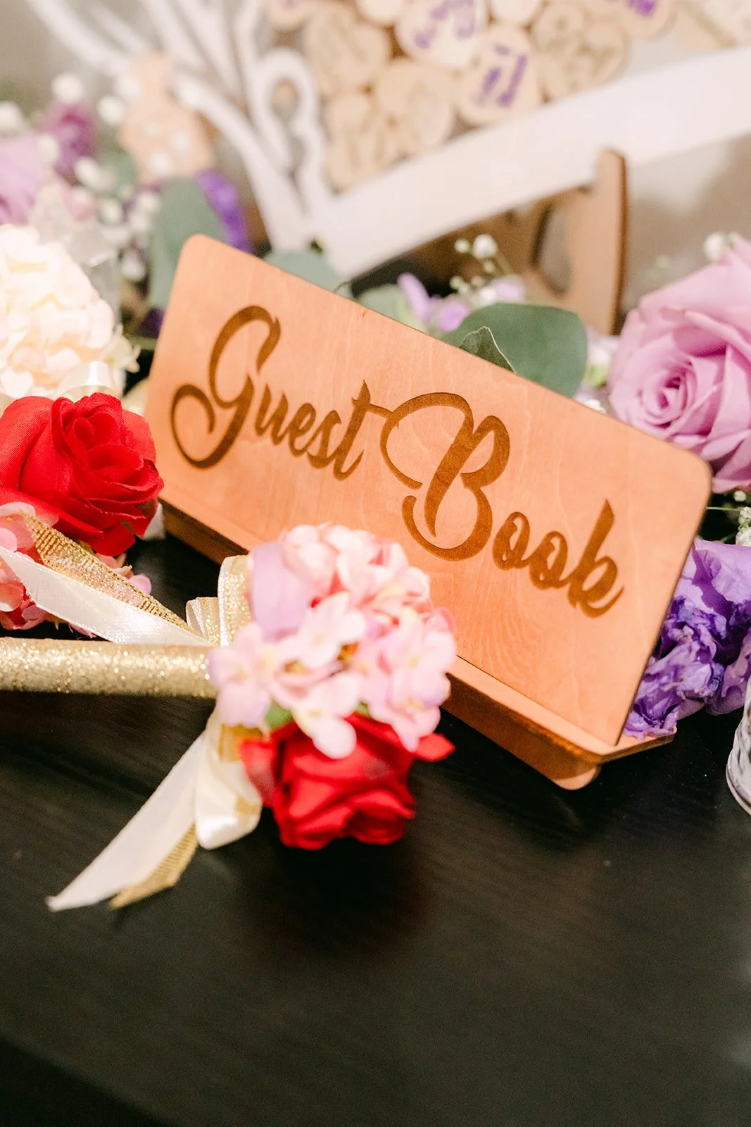 A wooden guest book sign with pink and red florals.