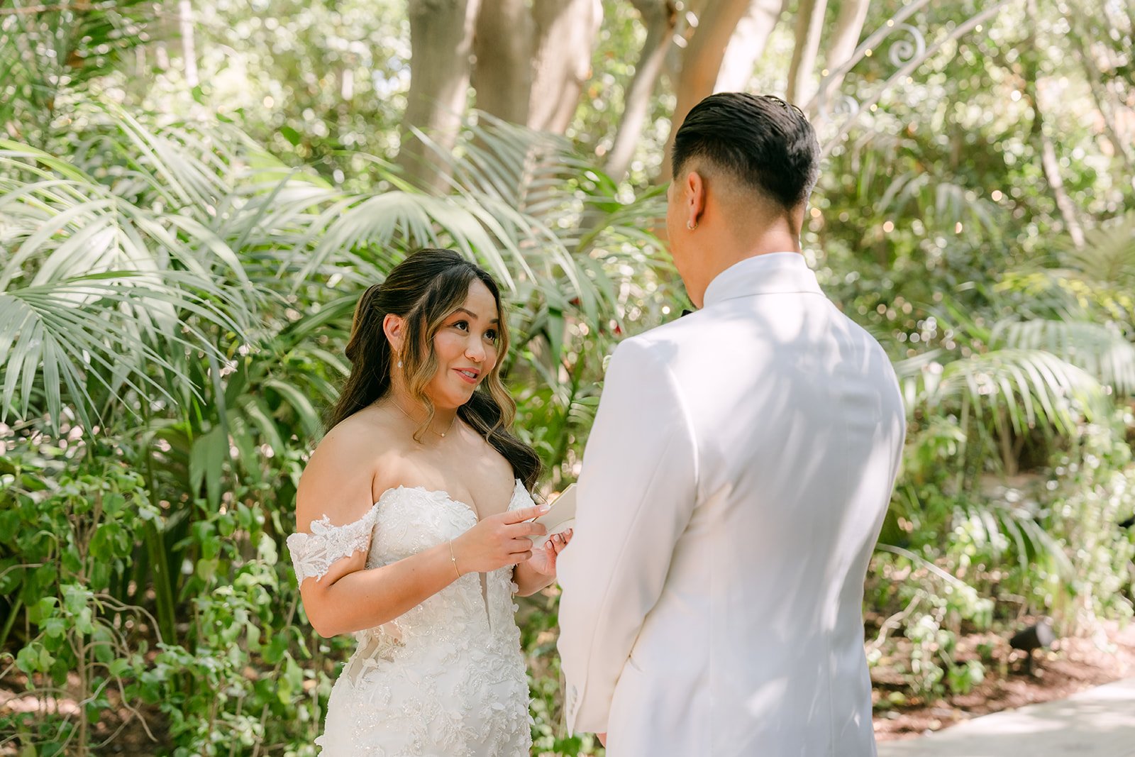 Nicole smiling as she reads her vows to Caryl among the palms.