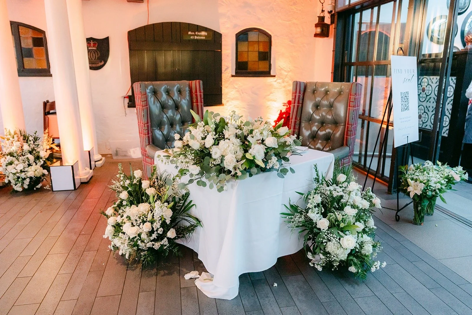 The sweetheart table with white flowers and grey wingback chairs