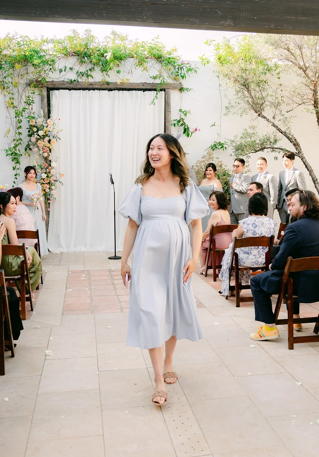 A bridesmaid in dusty blue walking down the courtyard aisle