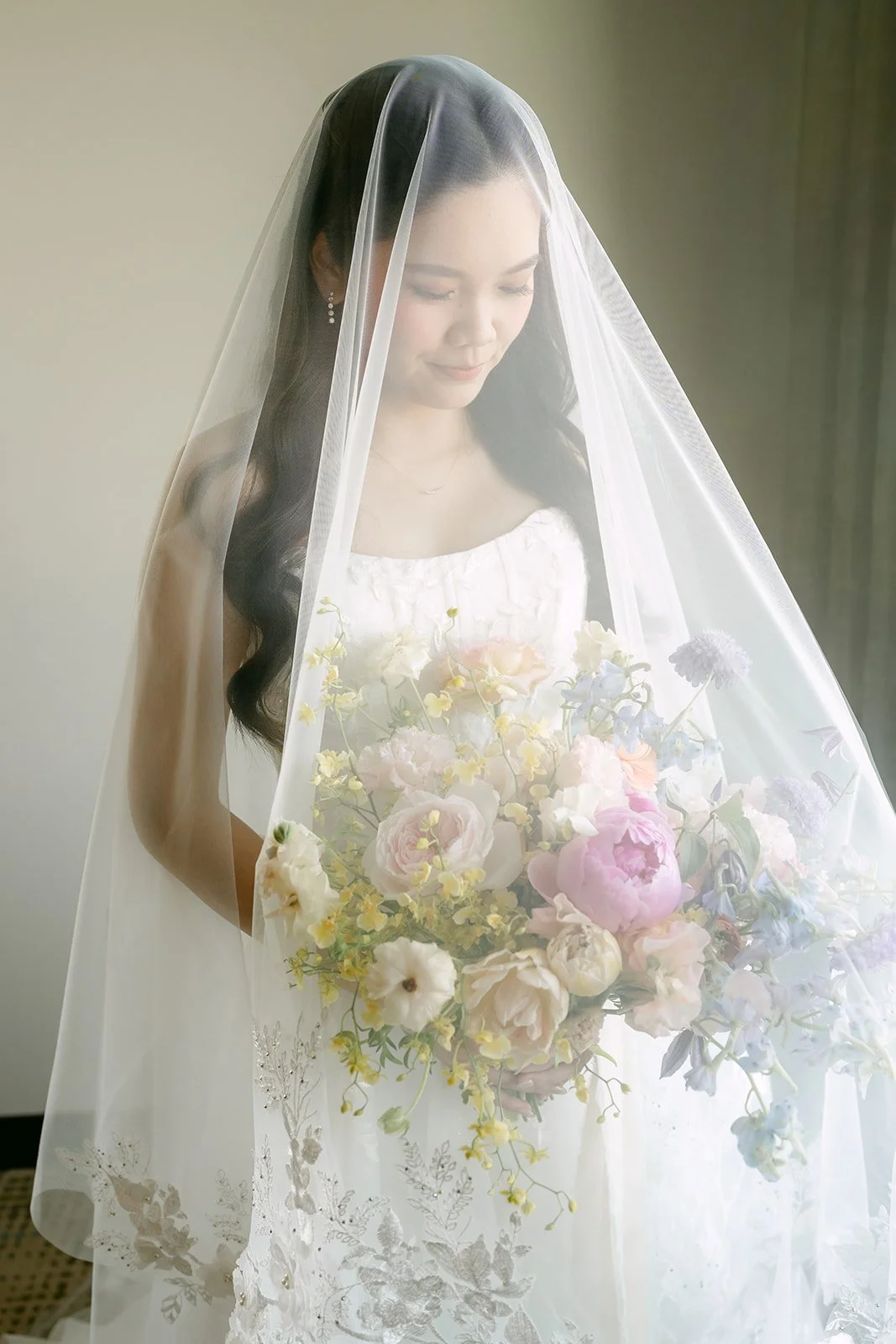 Bride under her veil holding a pastel rainbow bouquet