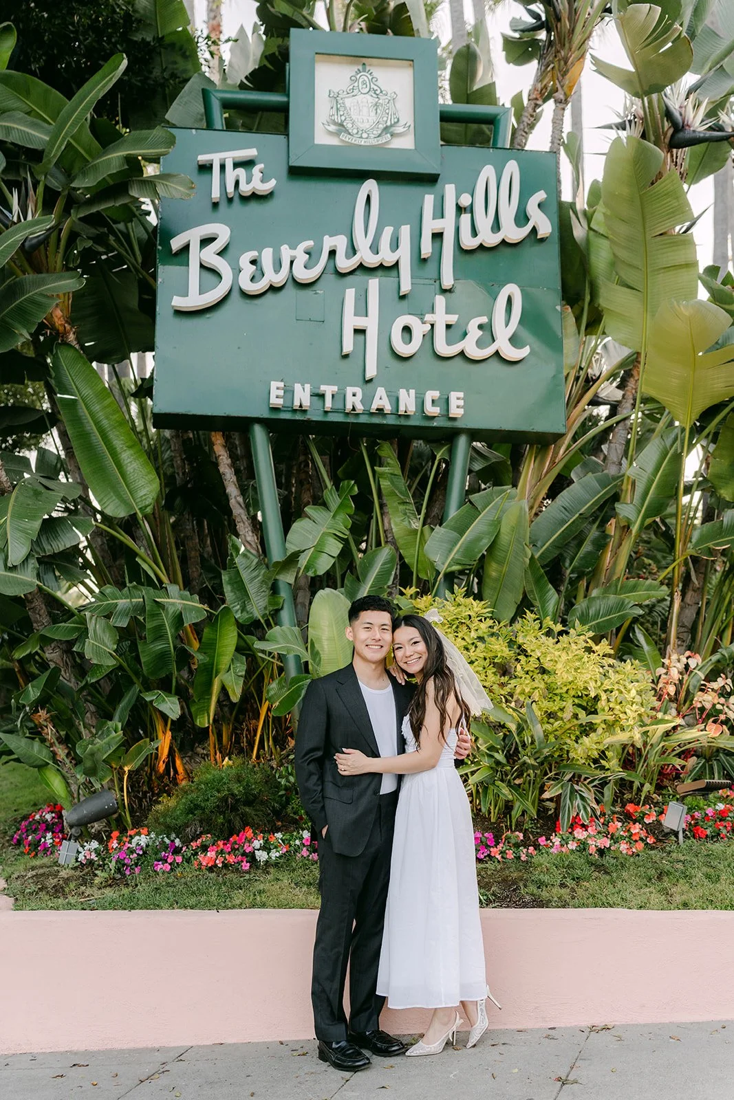 Jadee and Richard pose in front of the tropical plants and the hotel's entrance sign.
