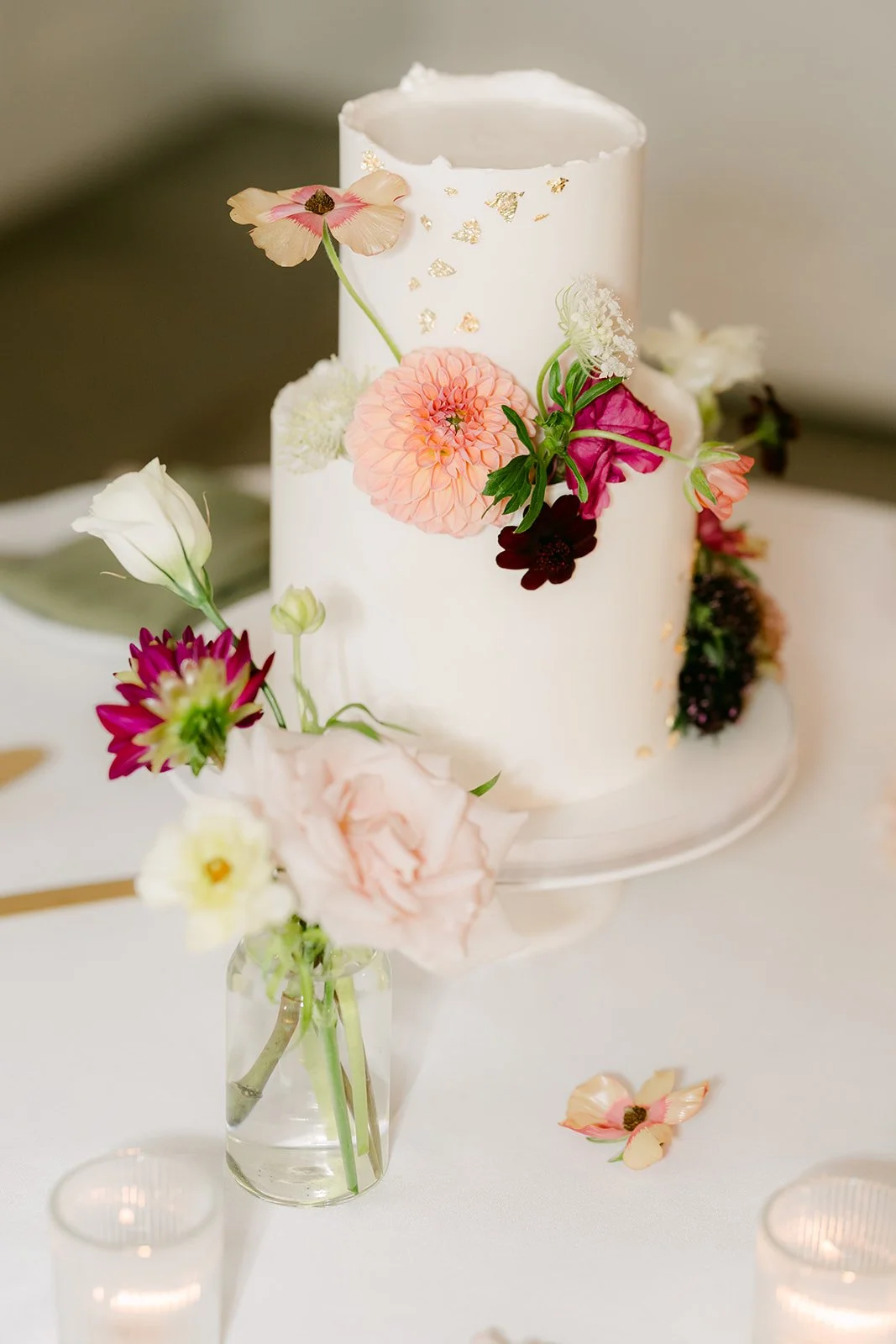 The cake with bud vases and candles on the cake table.