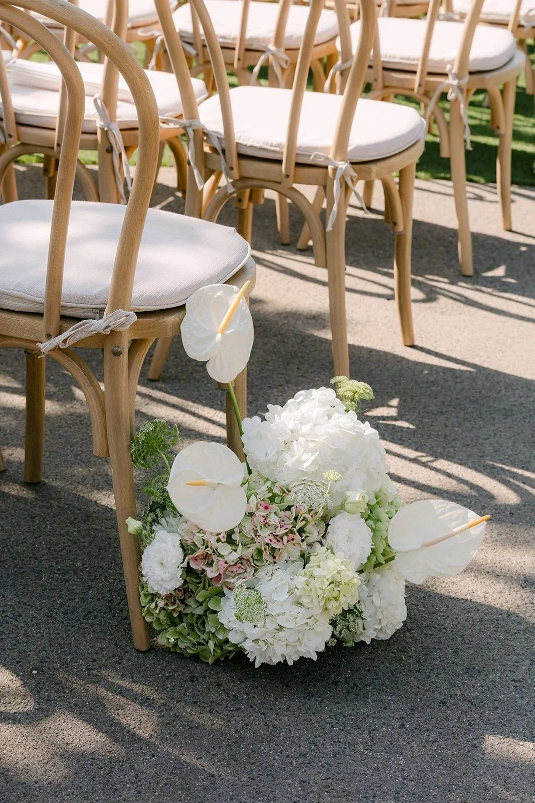 White orchid and hydrangea aisle arrangement beside wooden chairs