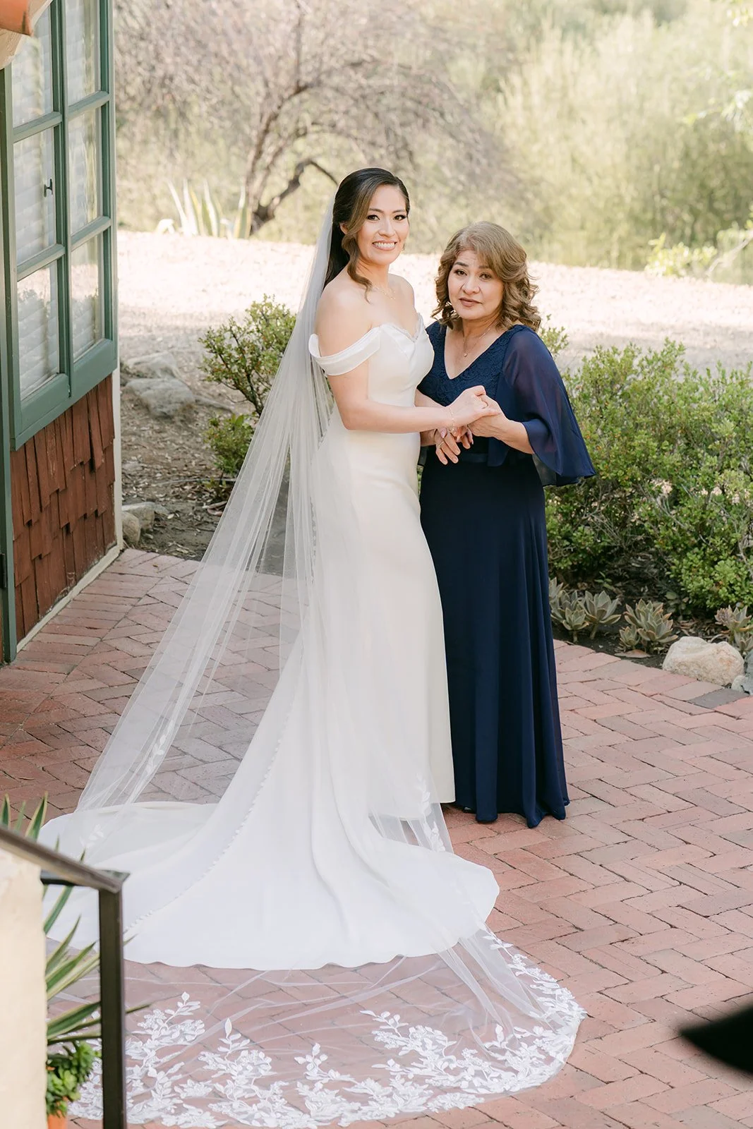 Mariana and her mom with her cathedral lace veil spread across the brick path, photographed by One and Only Production