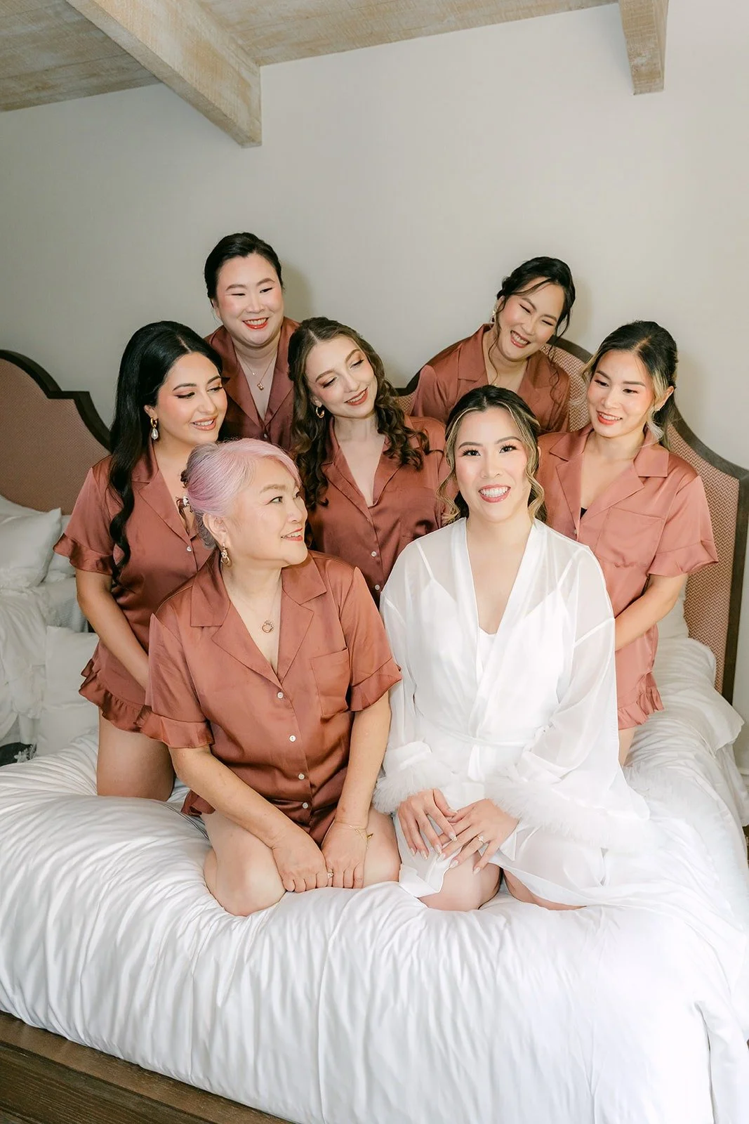 Joanne and her bridesmaids in matching satin pajamas laughing together on the bed