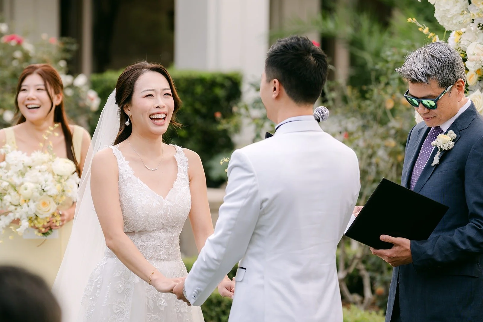 Jenny laughing as she holds Ryan's hands while officiant Jason Poon speaks.