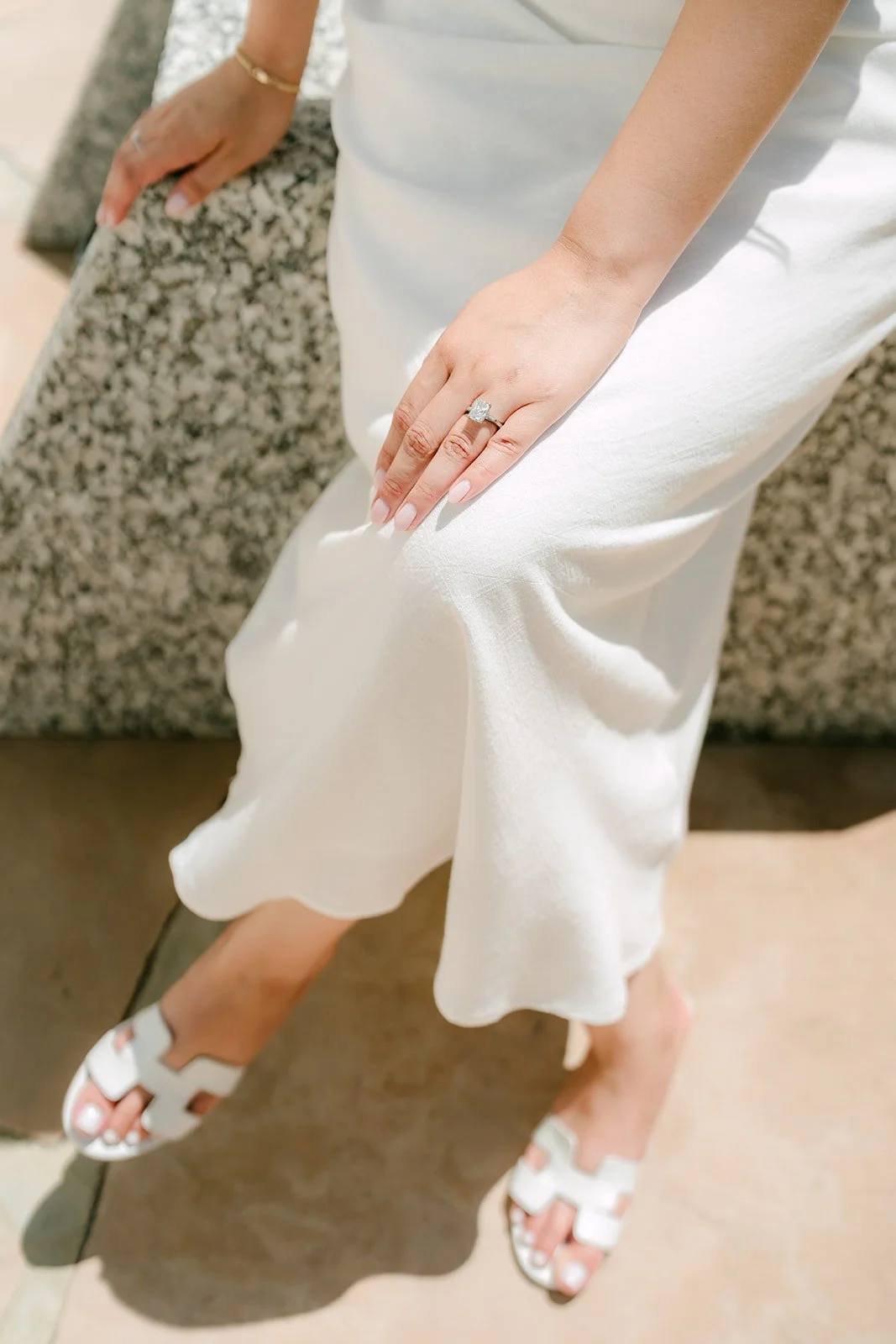 Detail of Stephanie's engagement ring as she sits on a granite block.