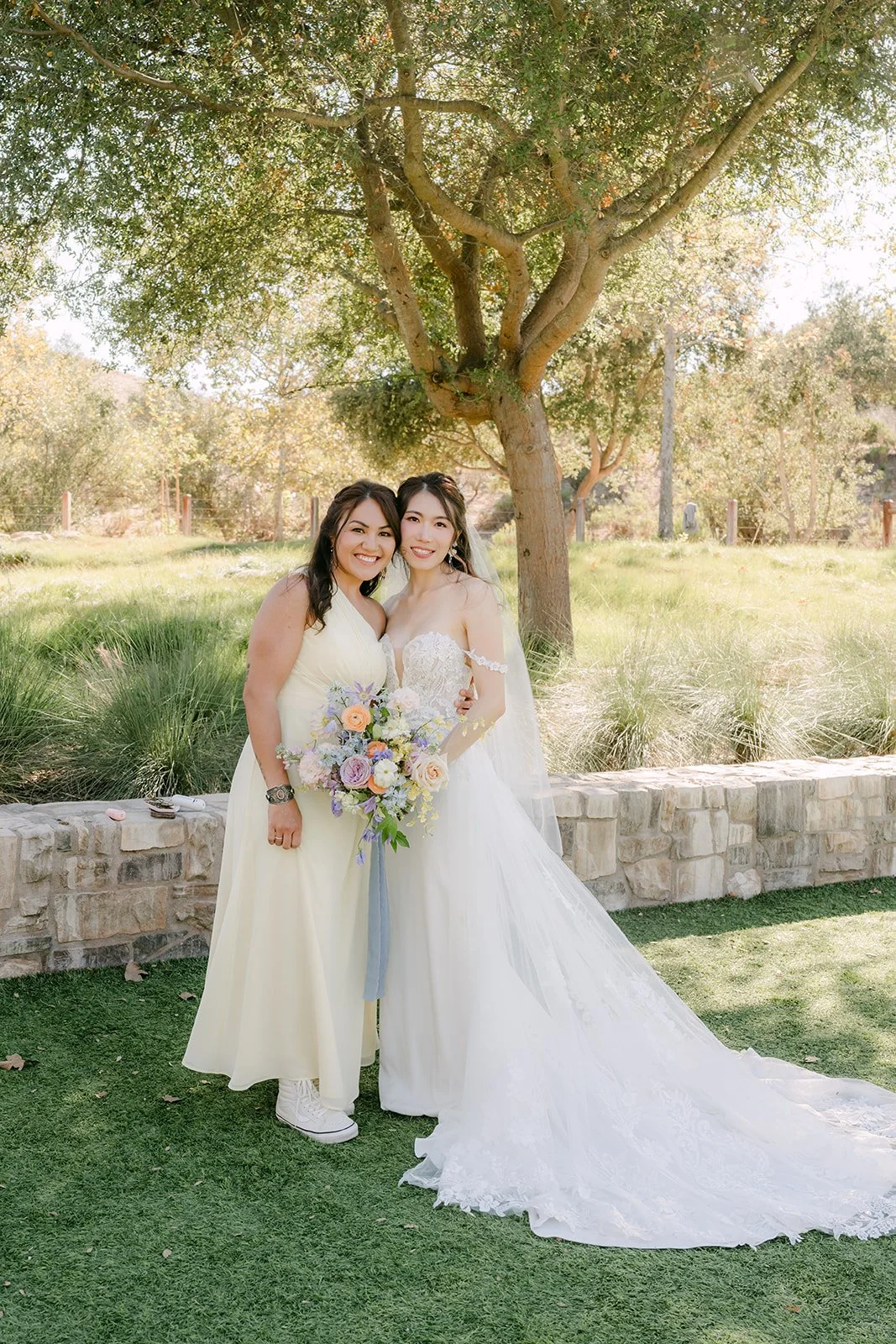 Christie and a bridesmaid posing together under the trees.