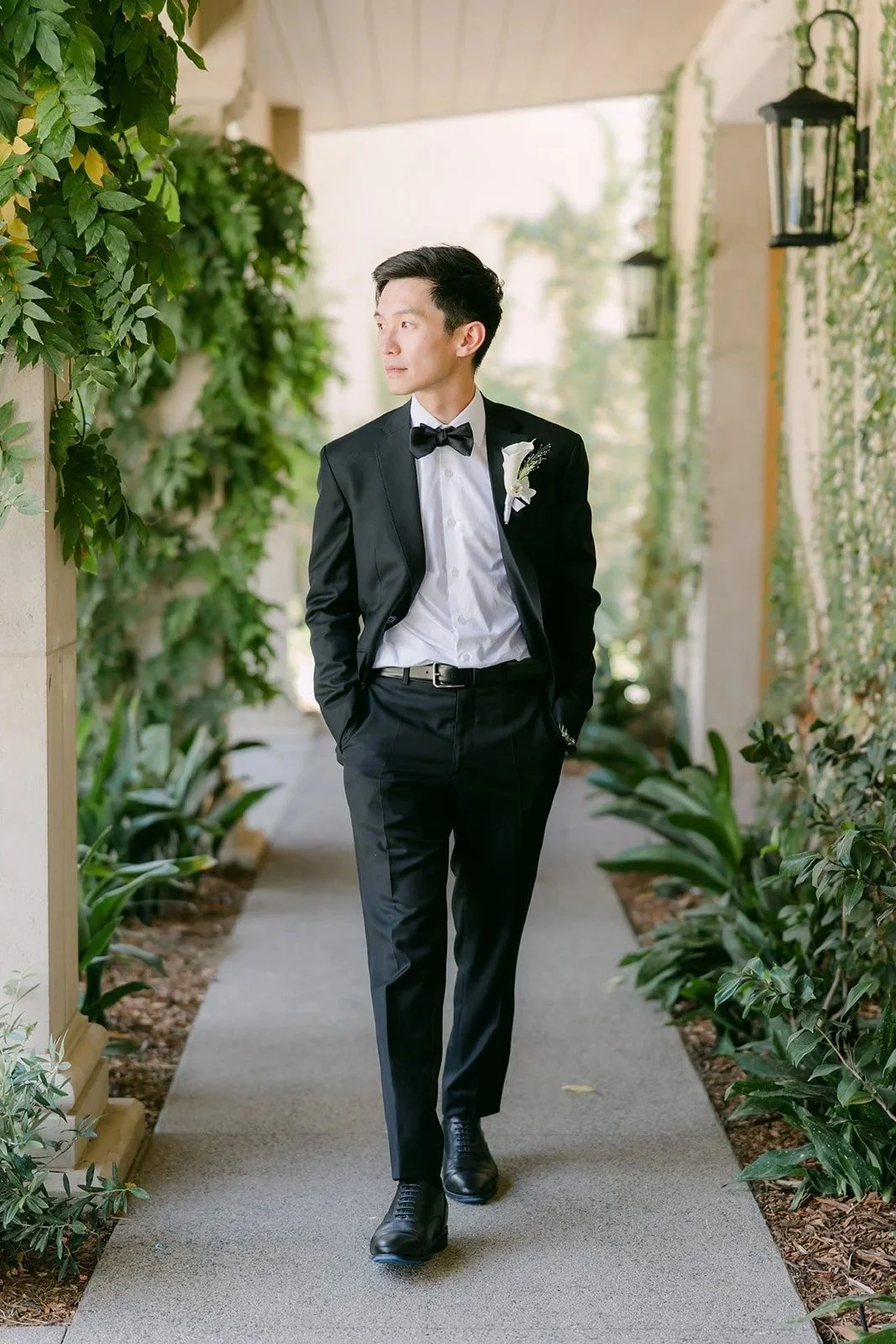Tyler walking down the ivy covered loggia in a black tuxedo