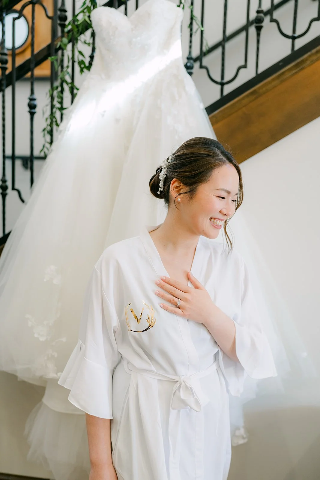 Bride in her robe laughing in front of her gown on the staircase