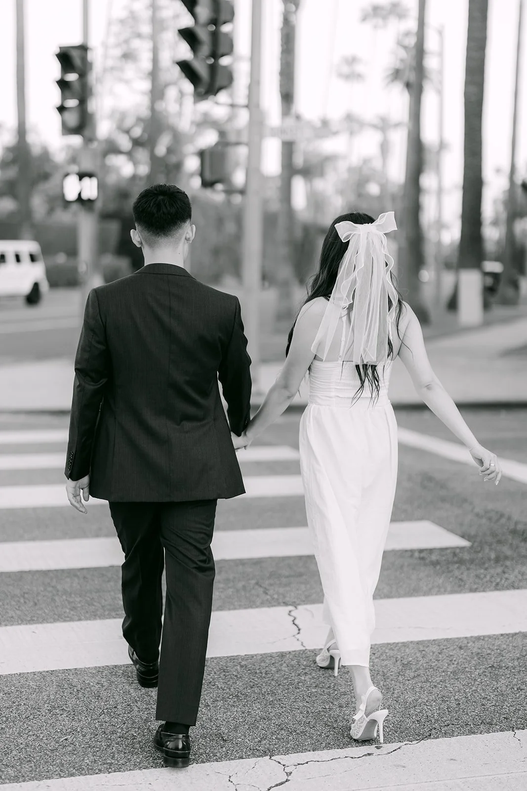 Black and white photo of Jadee in a veil walking hand in hand with Richard across the crosswalk.