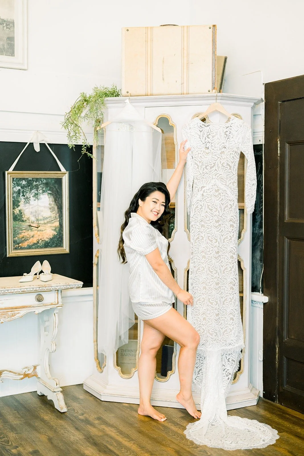 Hannah in her robe beside her lace gown hanging in the bridal suite