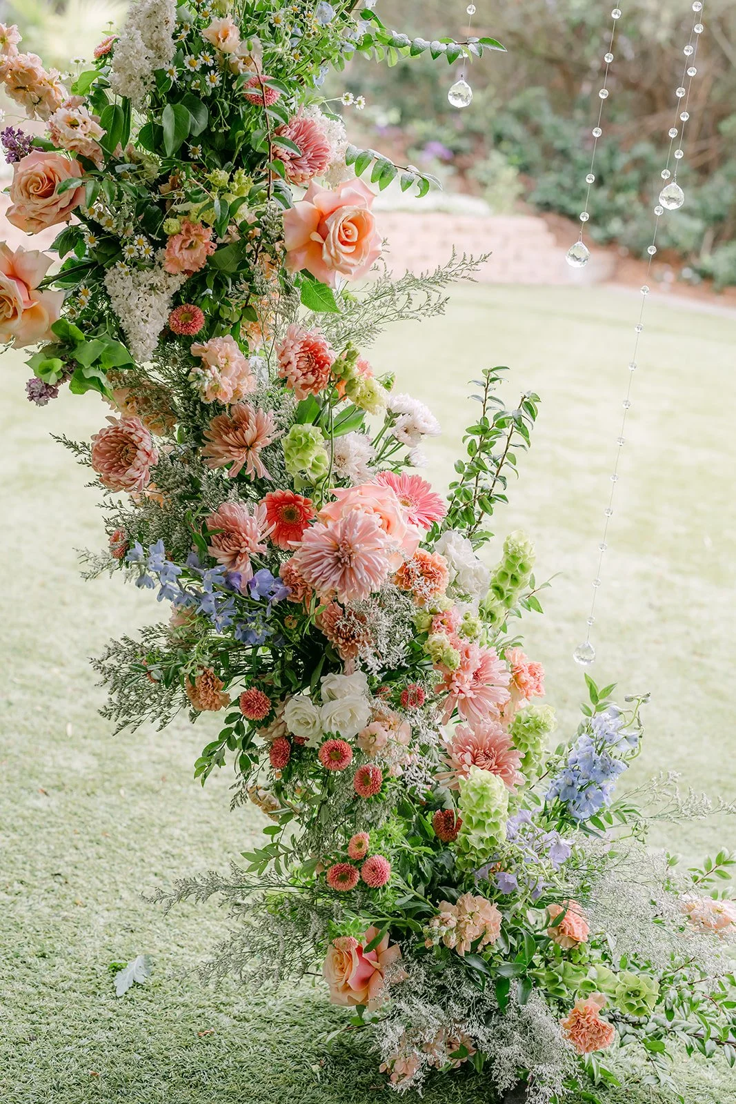 Pastel floral column of roses and dahlias at the ceremony arch