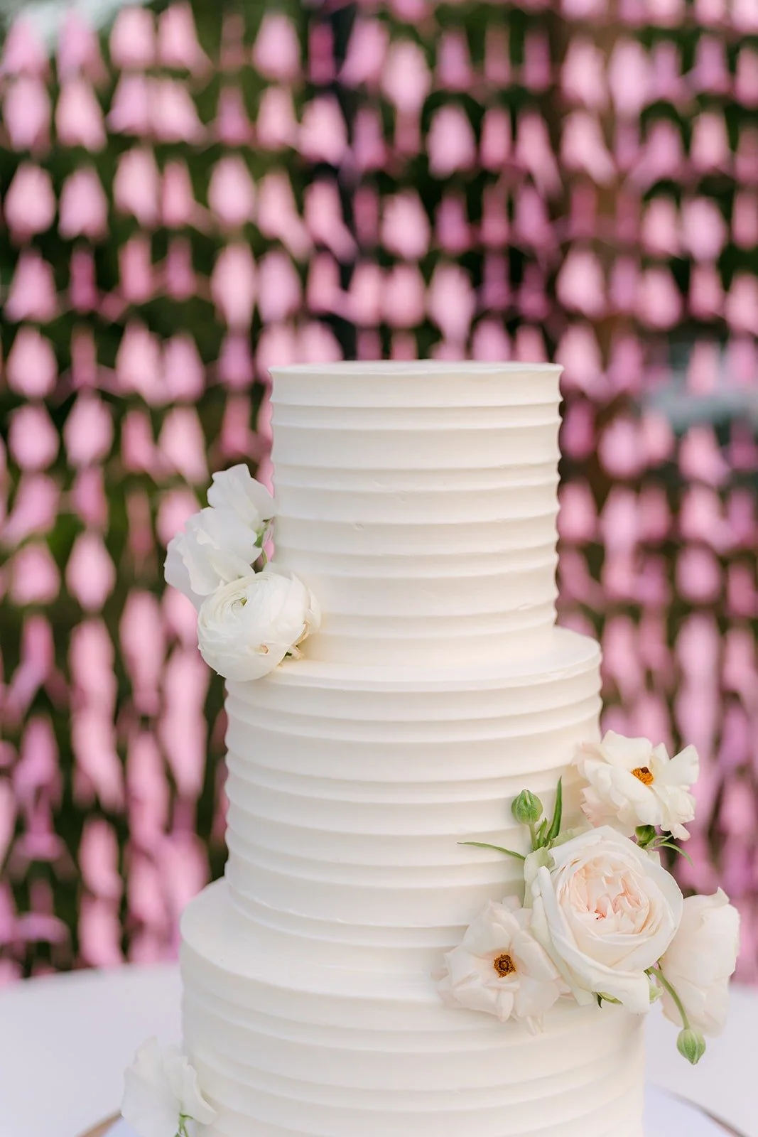 The white three tier Sugar Lab cake with ivory flowers in front of pink paper cranes