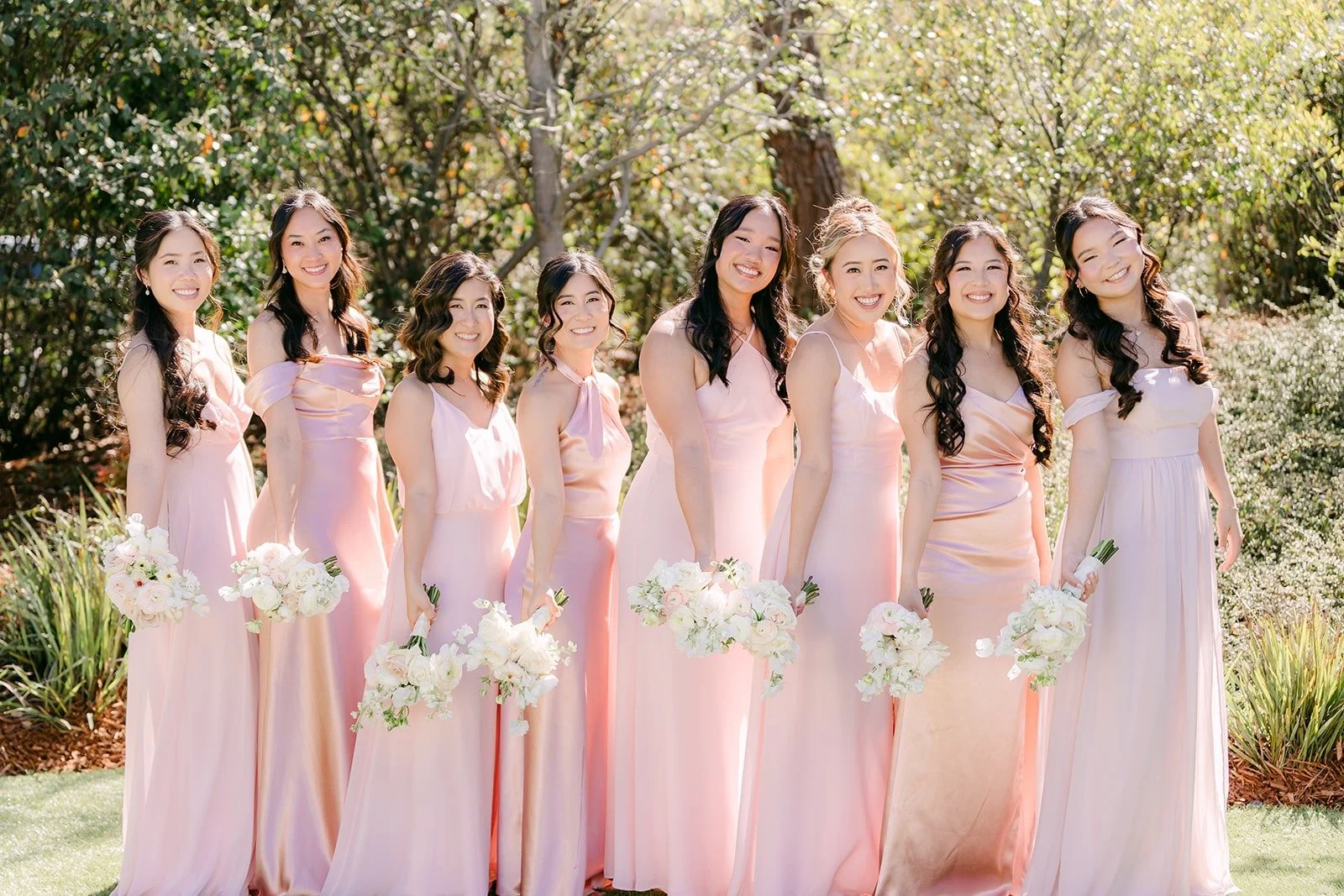 Kelli and her bridesmaids in blush dresses holding their bouquets in the garden