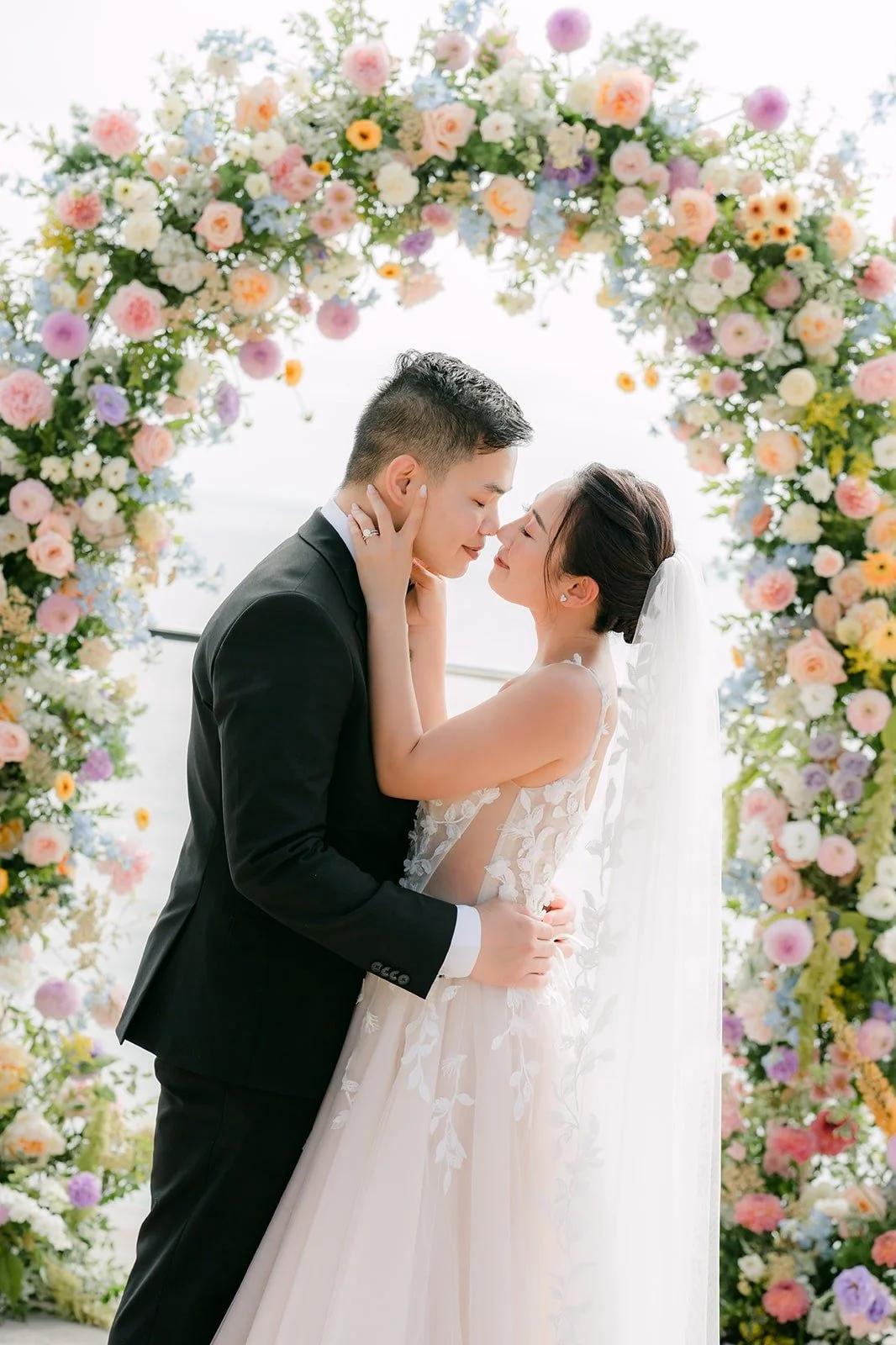 Mario cupping Kylie's face under the floral arch
