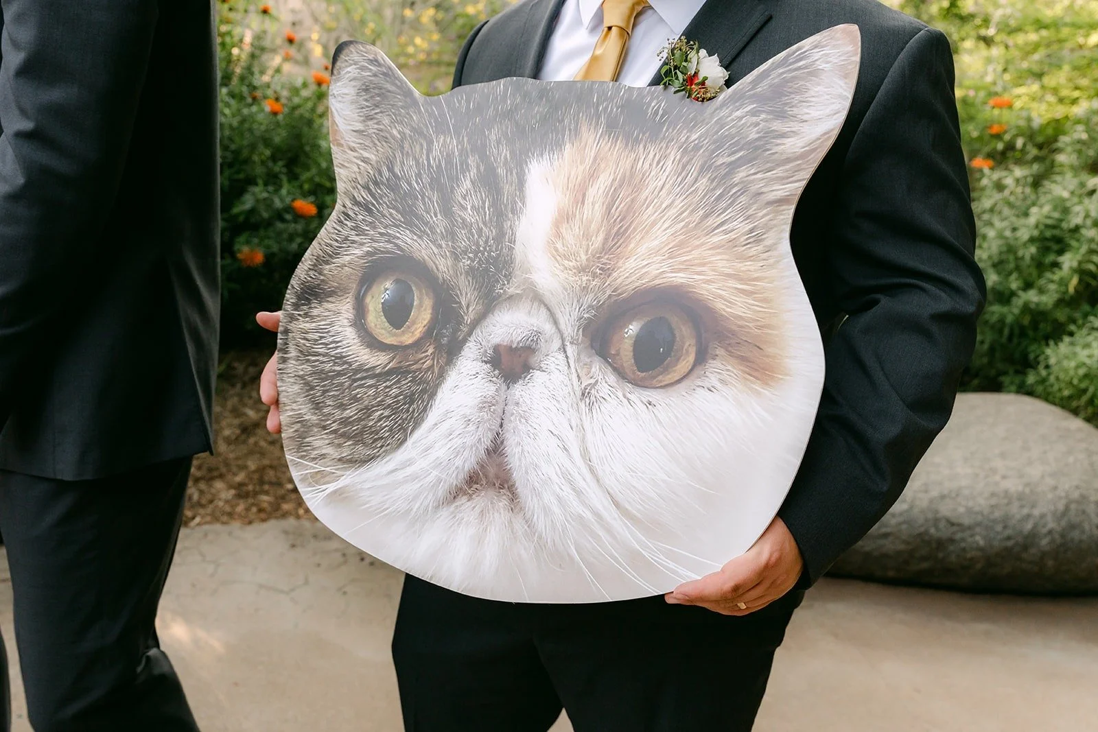 A groomsman holding up a big cat face cutout in front of his jacket