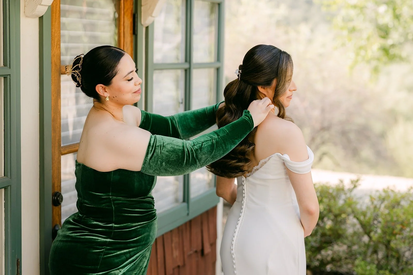 A bridesmaid in green velvet helping Mariana into her gown