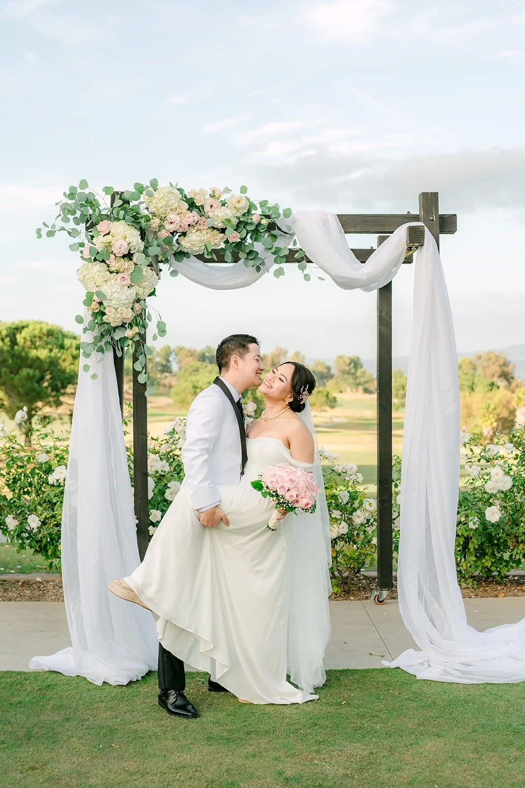 Ivy and Chungman under the white draped ceremony arch