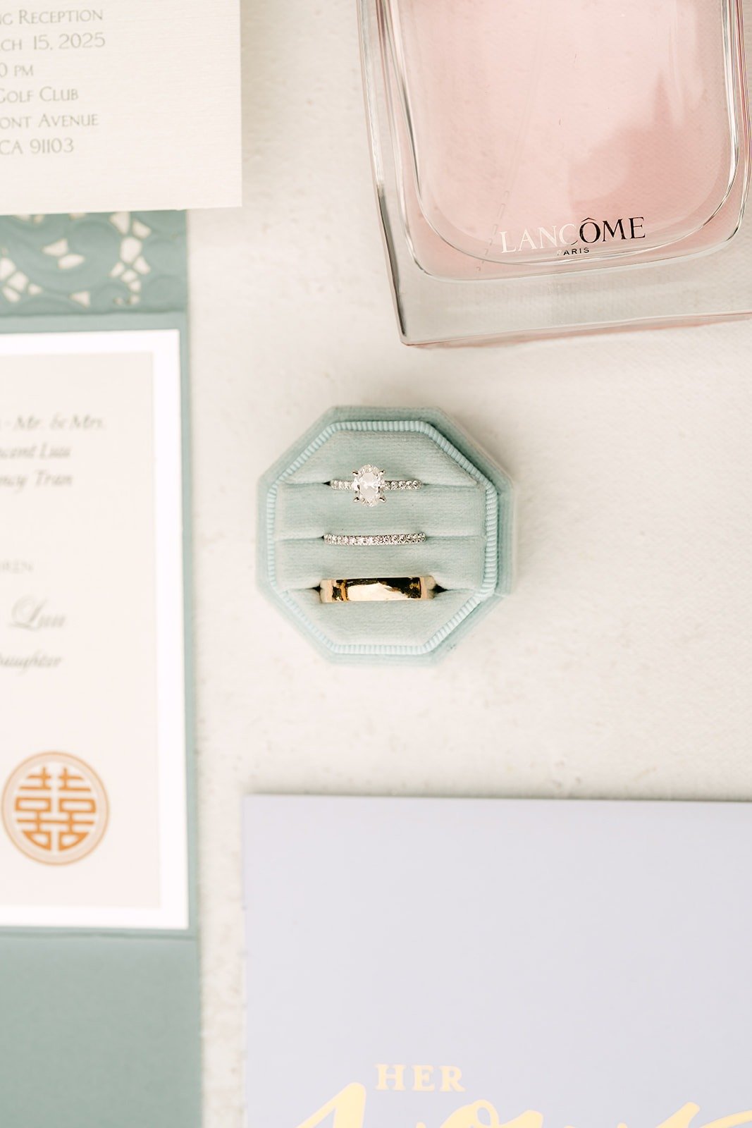Wedding bands in a dusty blue velvet ring box beside the invitation
