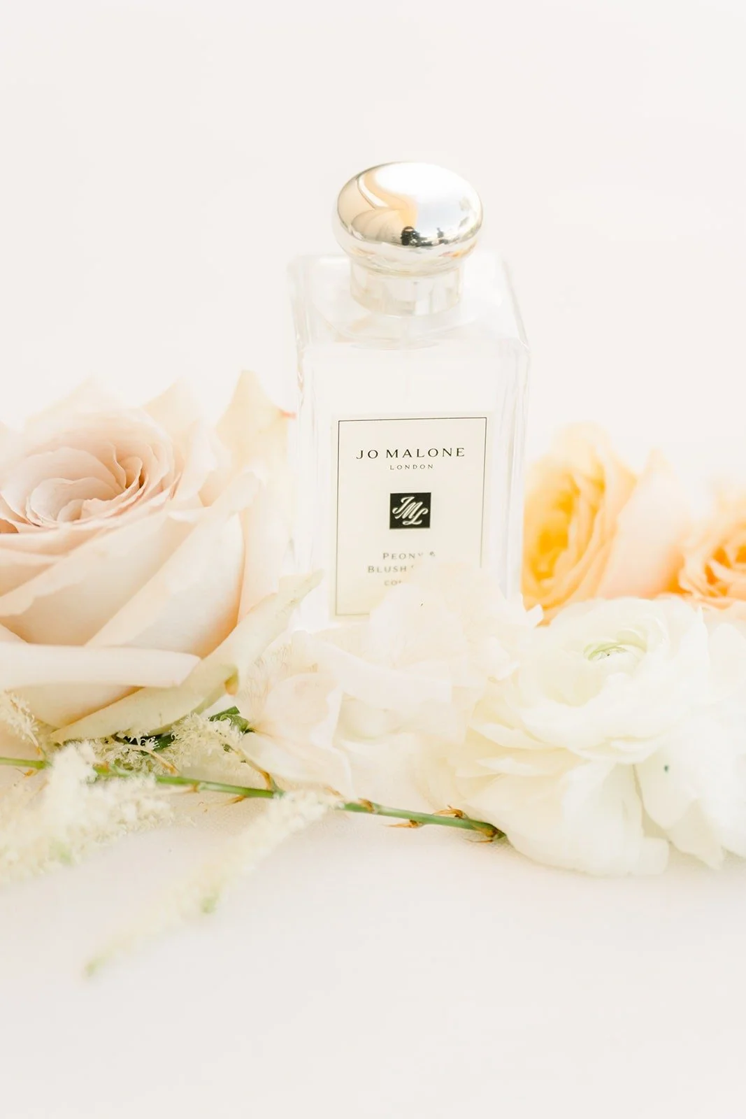 A bottle of perfume resting among cream roses