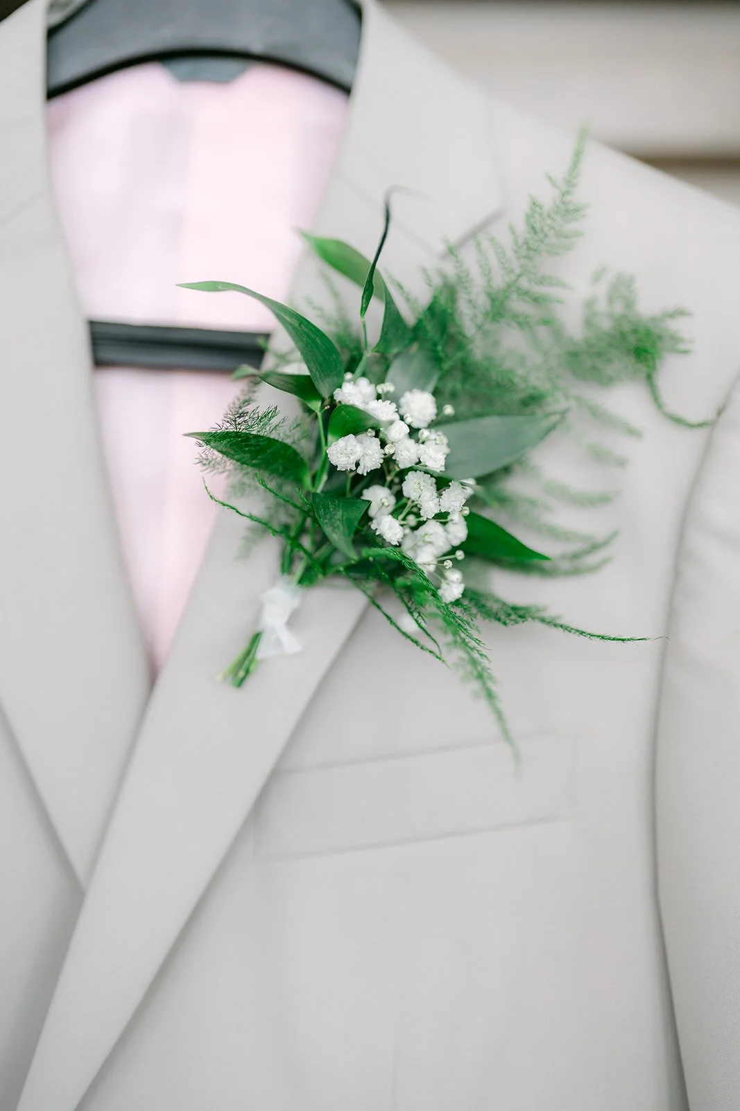White and greenery boutonniere on a tan suit lapel