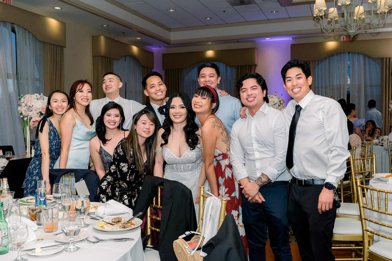 Guests gathered around a reception table for a group photo, photographed by One and Only Production