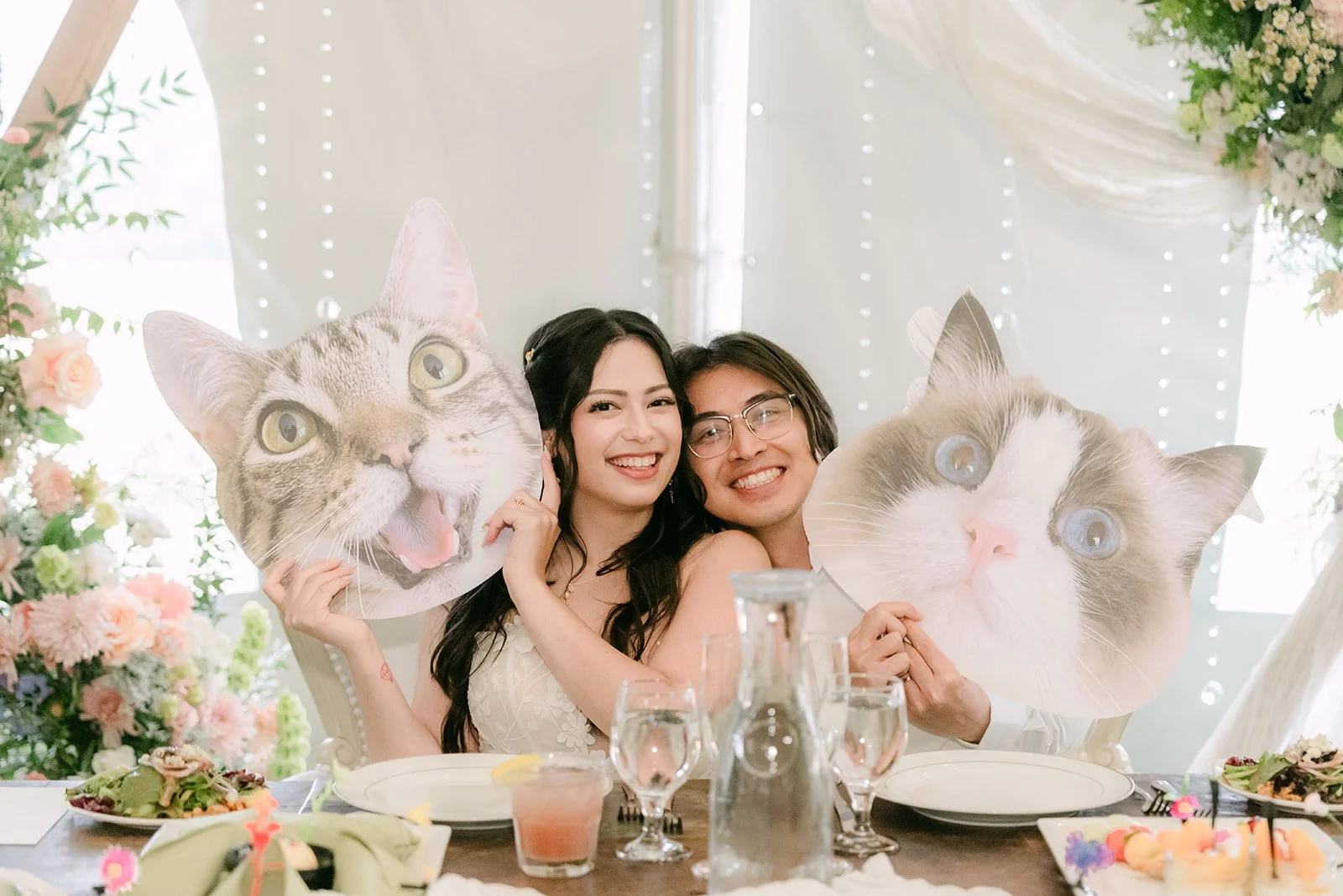 Kat and Mike laughing at the sweetheart table with their cat face cutouts
