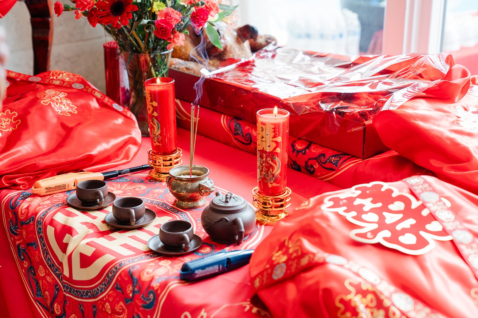 Red teacups and a tea set on a double happiness tablecloth.