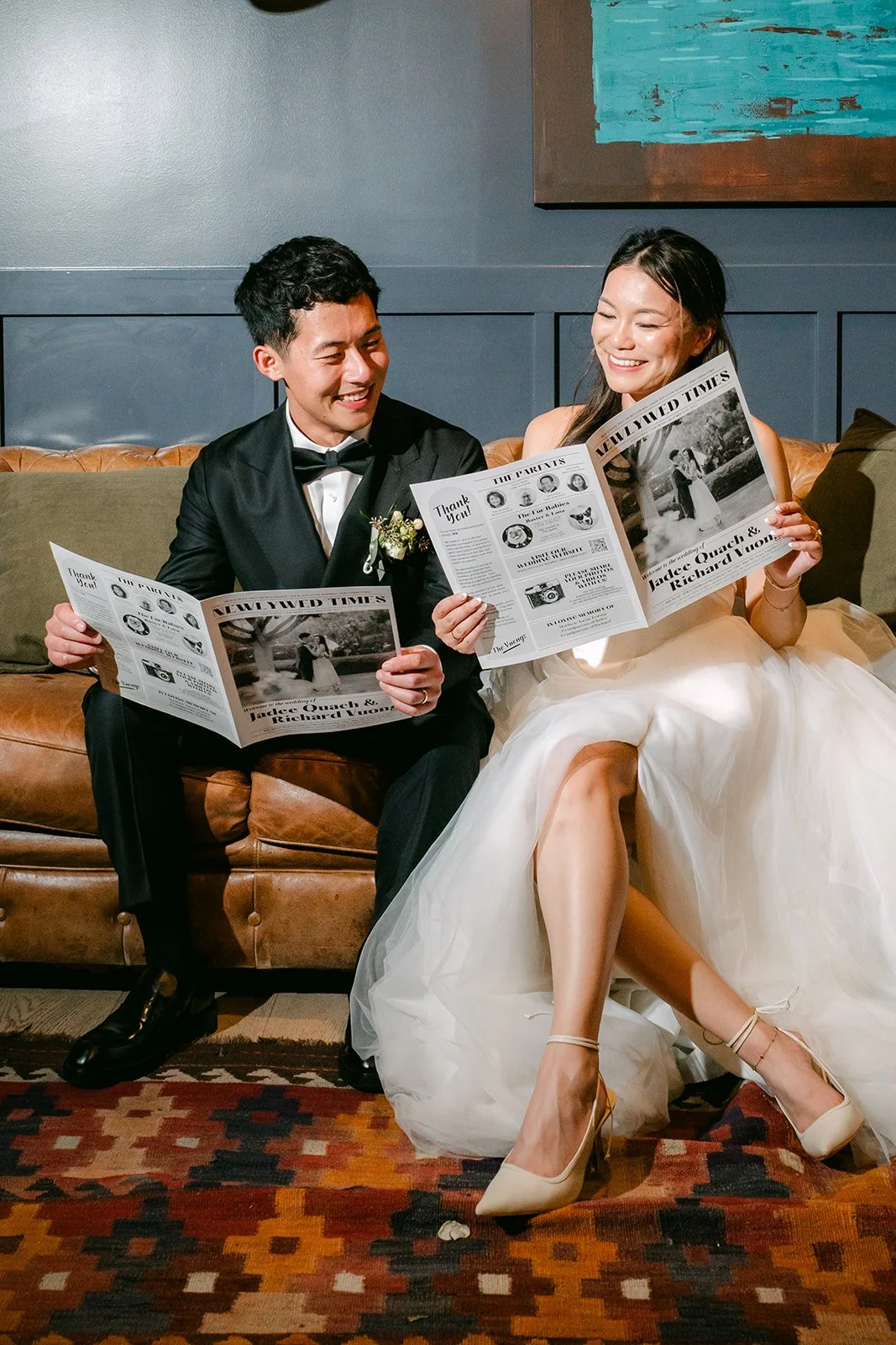 Jadee and Richard on the leather sofa with wedding newspapers in the library suite