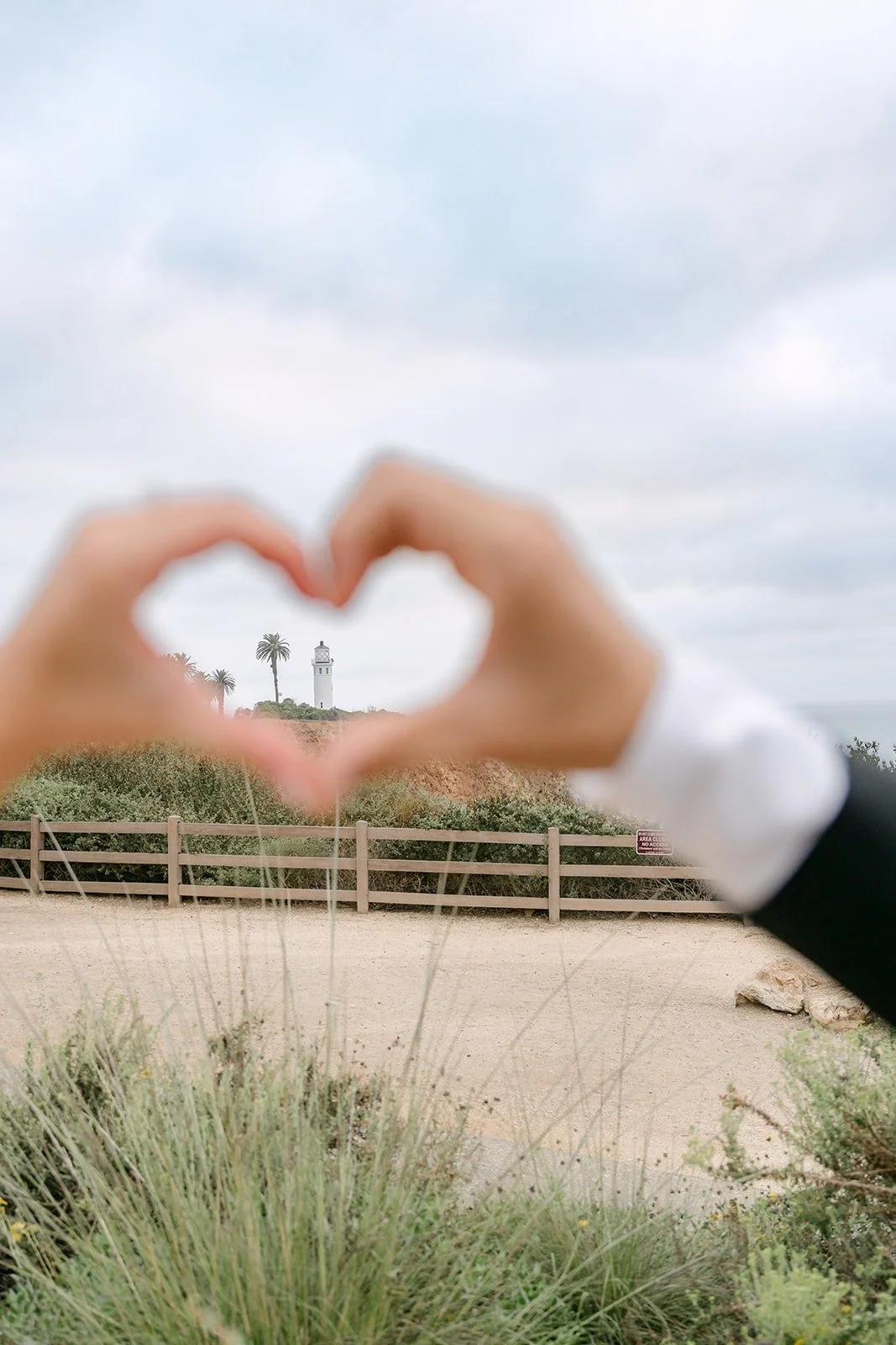 Kim and Vincent making a heart with their hands against the ocean