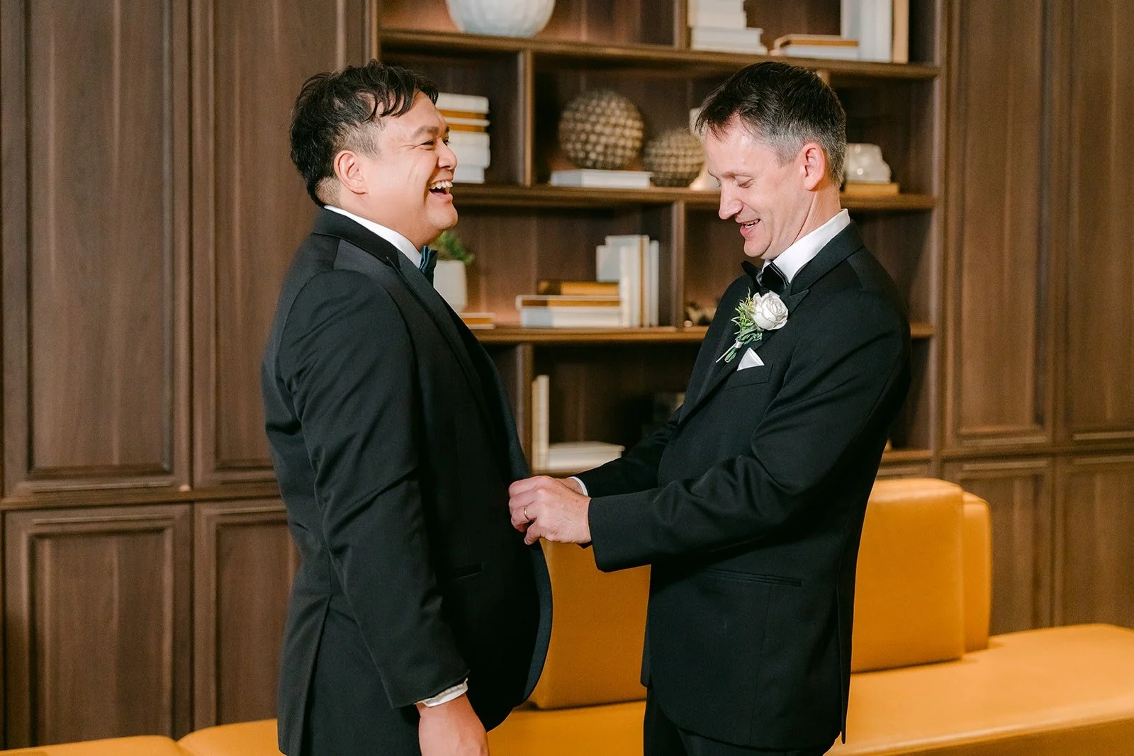 A groomsman pinning James's boutonniere in front of the bookshelves