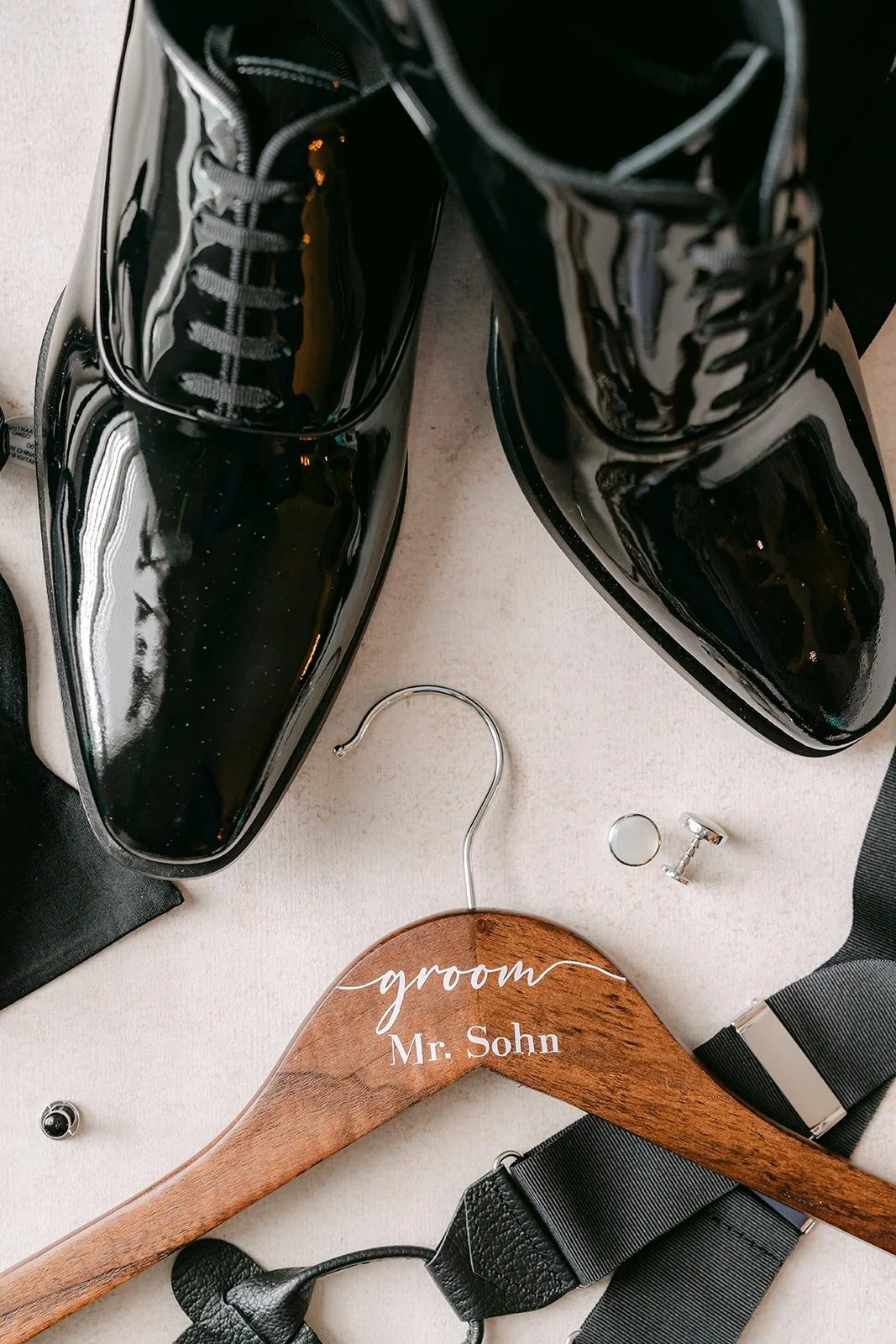William's patent leather shoes and bow tie beside an engraved wooden groom hanger