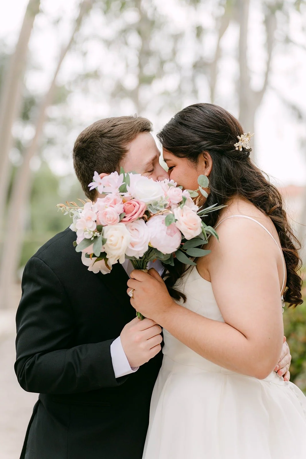 Saira and Matthew sharing a kiss behind her blush rose bouquet