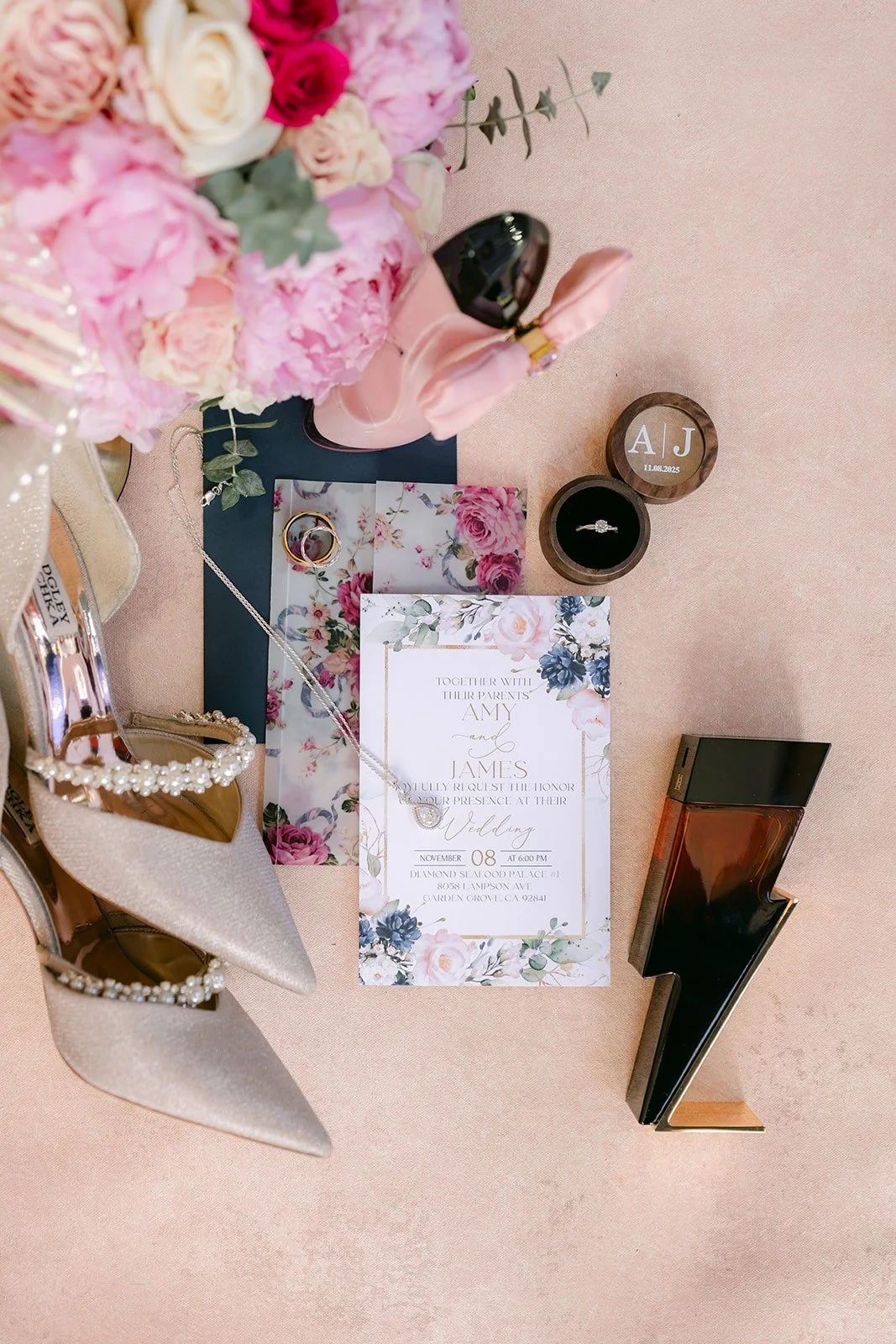 Flat lay of Amy's invitation suite, pearl heels, rings and pink peony bouquet on a blush backdrop