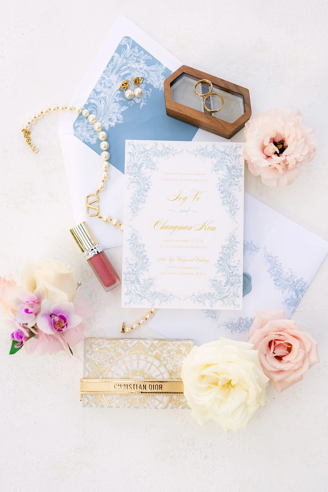 Ivy's invitation suite with pearls, perfume and blush roses on a dusty blue backdrop
