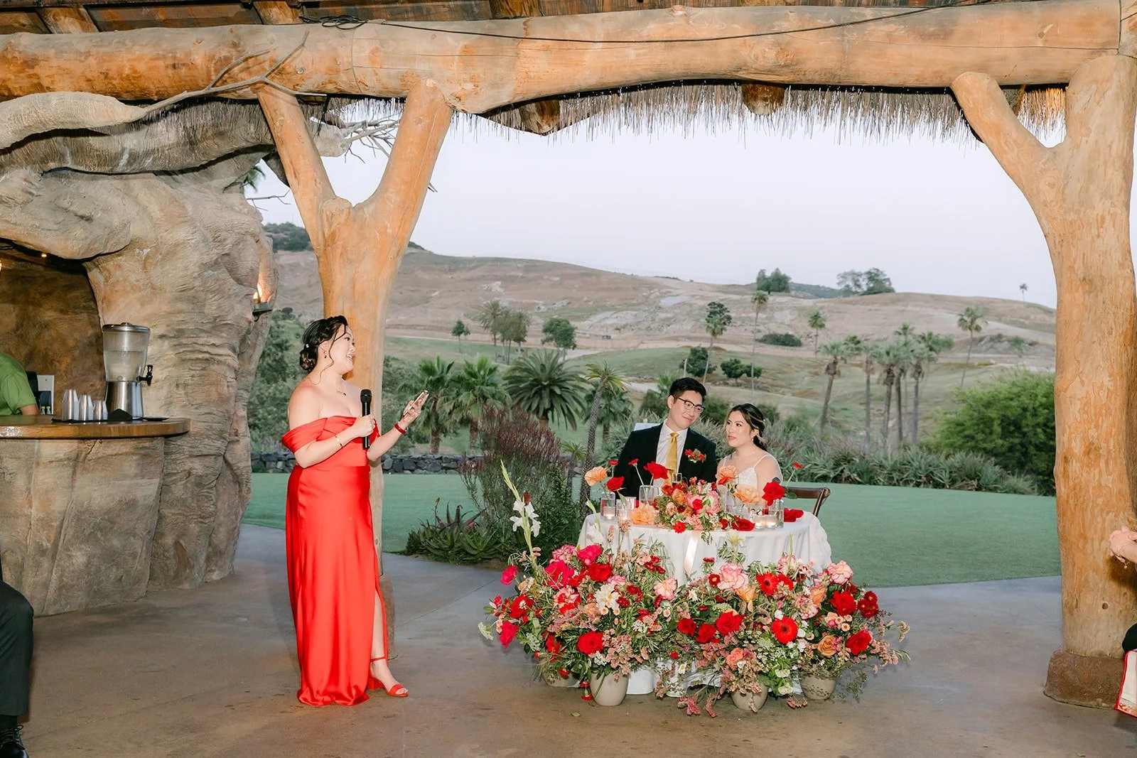 A bridesmaid in red giving a toast in front of the sweetheart table