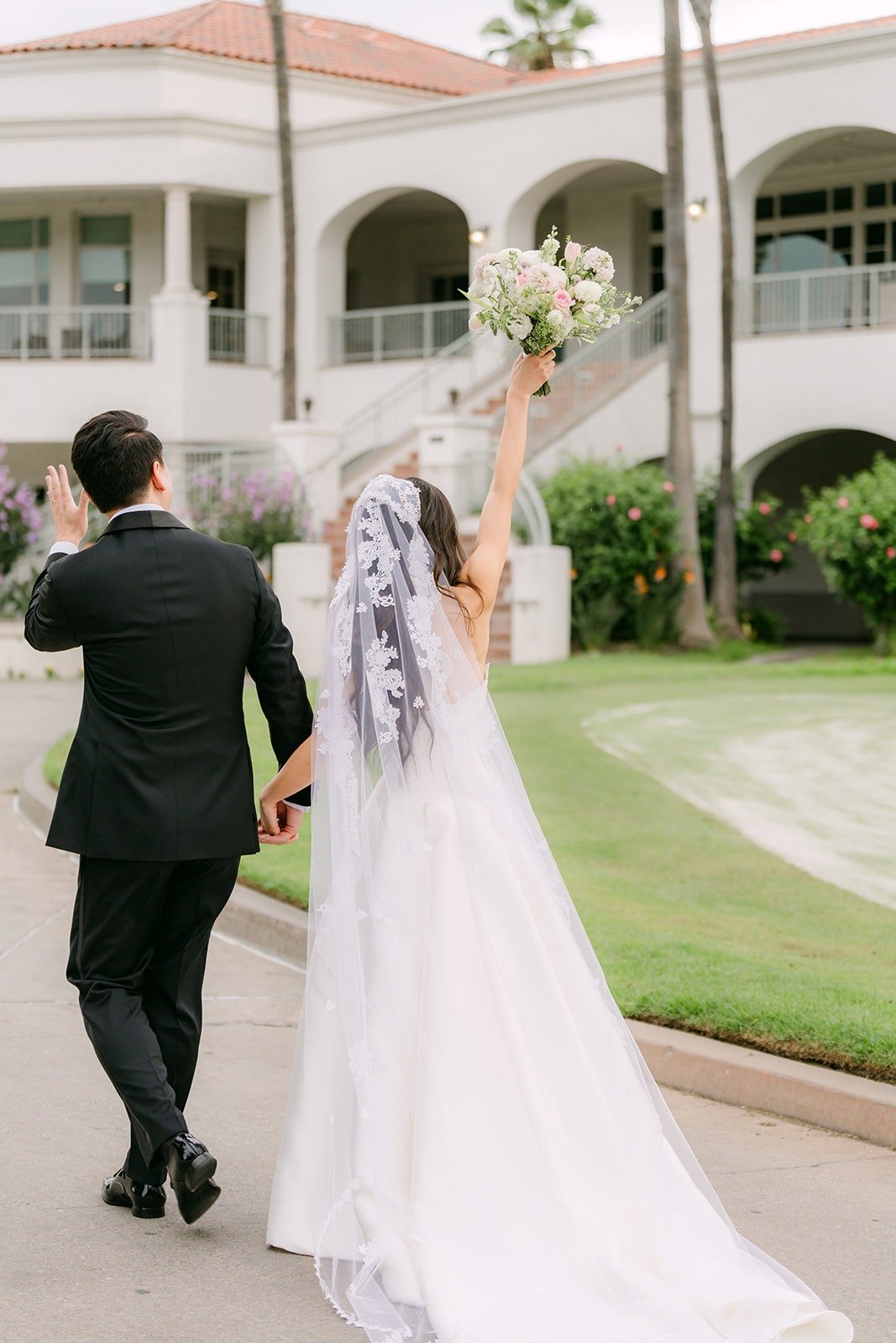 Kristine lifting her bouquet as William leads her up the clubhouse path